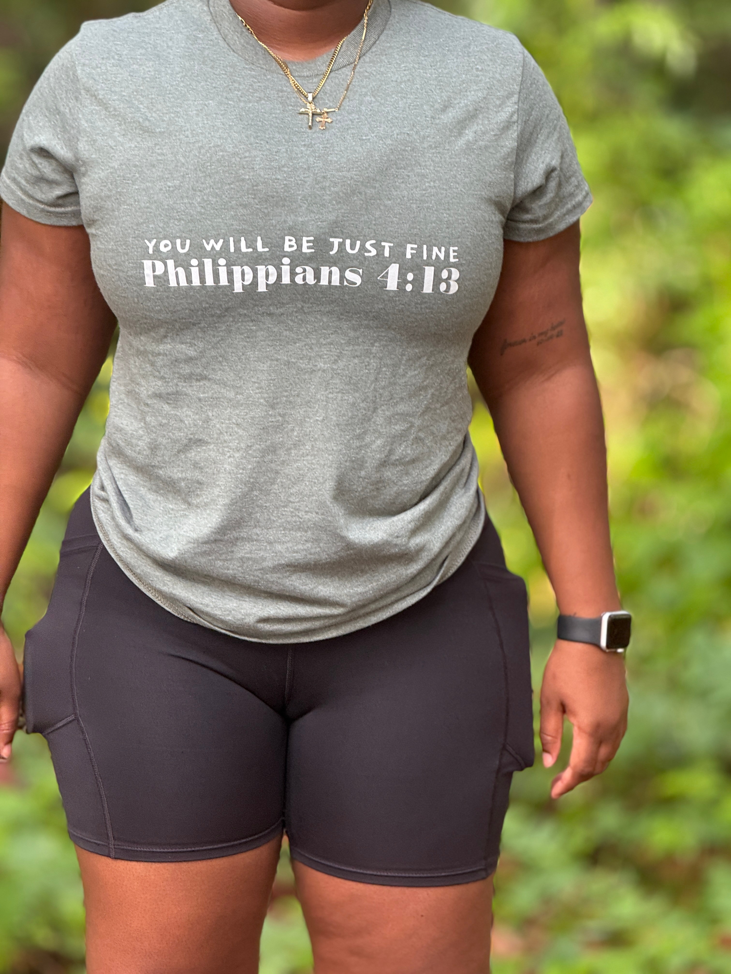 Person wearing a gray T-shirt with white text and black shorts, outdoors with green foliage background.