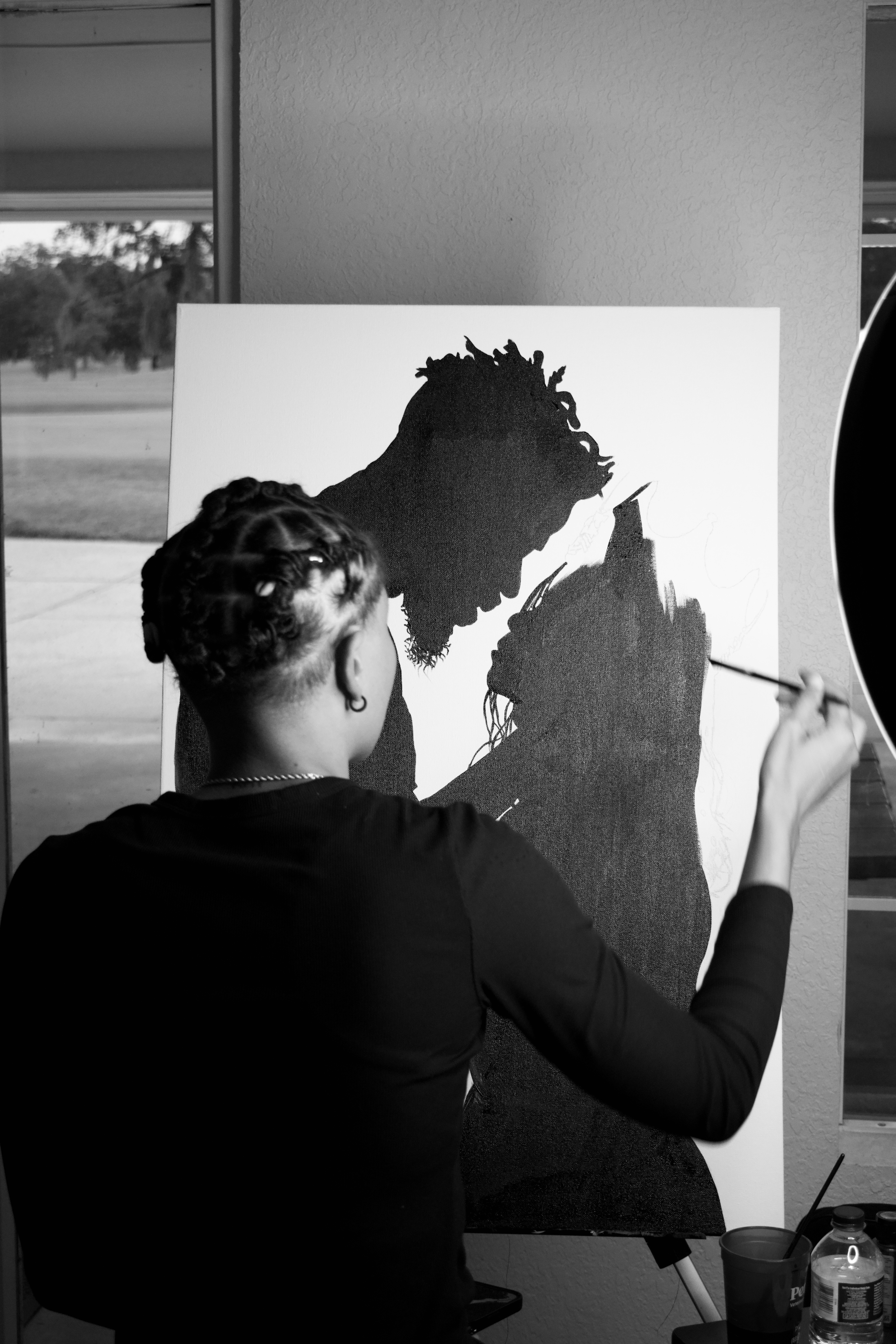 Person painting a silhouette of a dog on a canvas, with a window and outdoor scenery in the background.