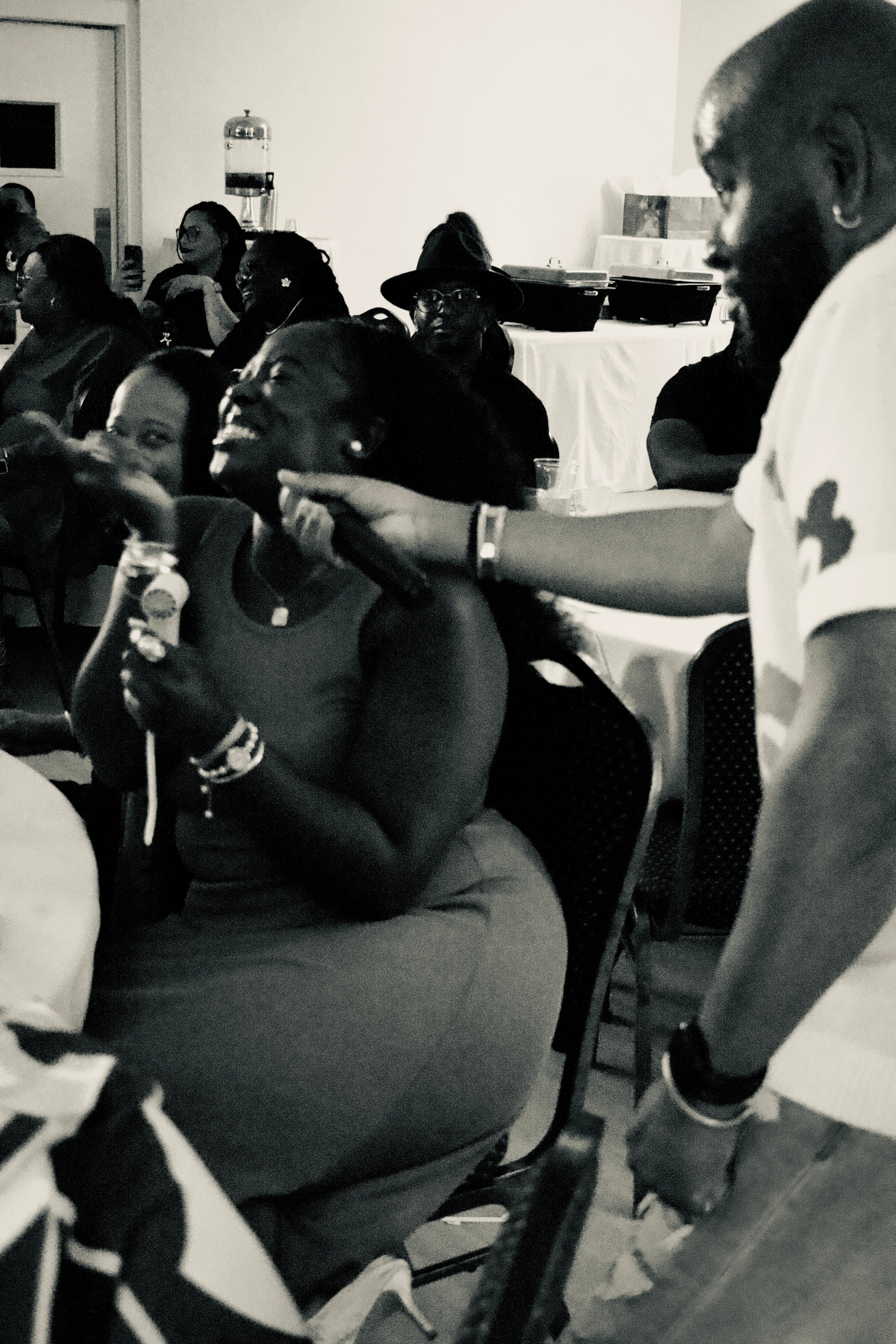 Group of people gathered indoors, some smiling and engaging with each other, with a woman holding a small object.