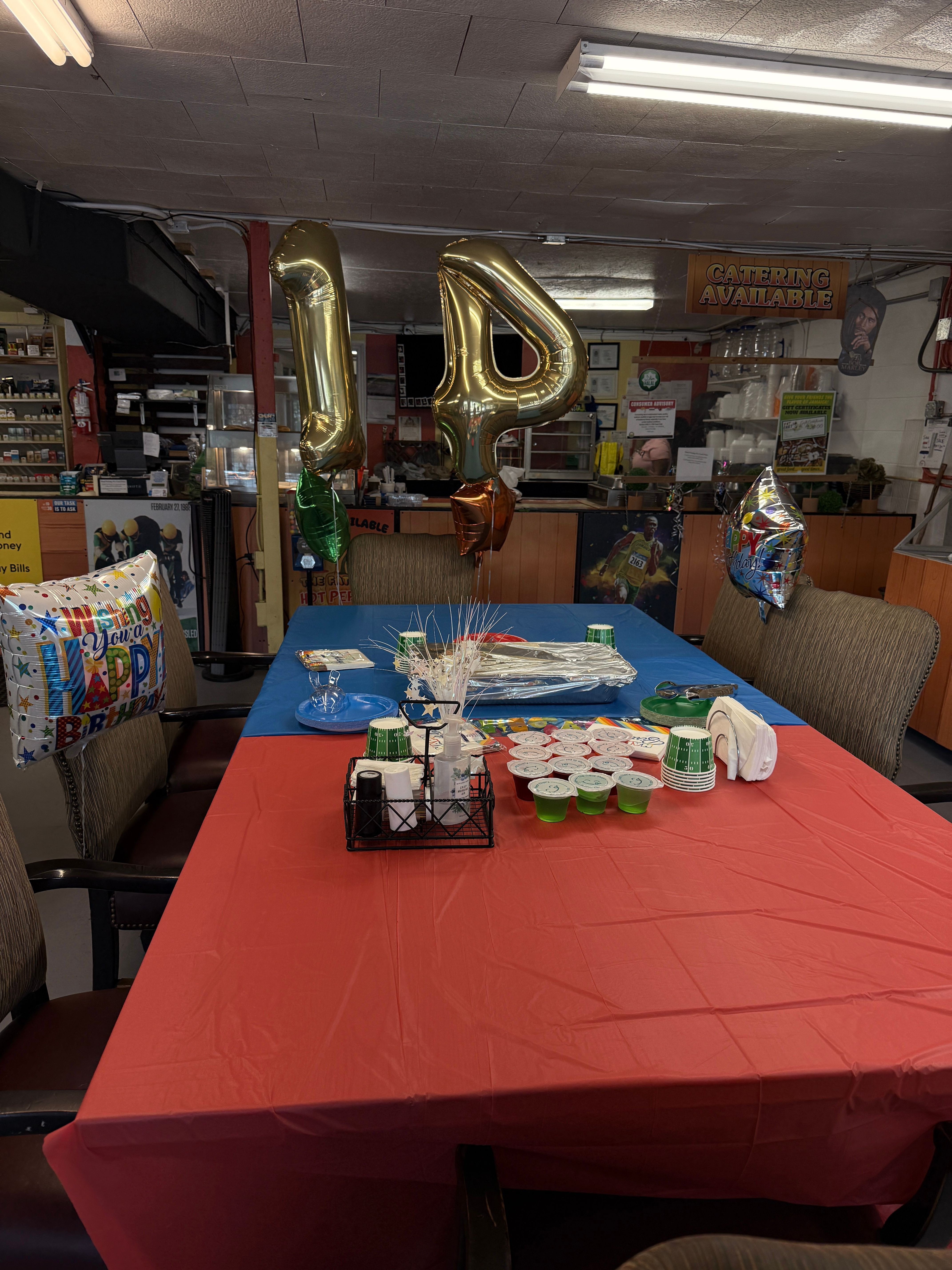 Party table with red and blue tablecloths, balloons, and cups, in a room with shelves and kitchen items.