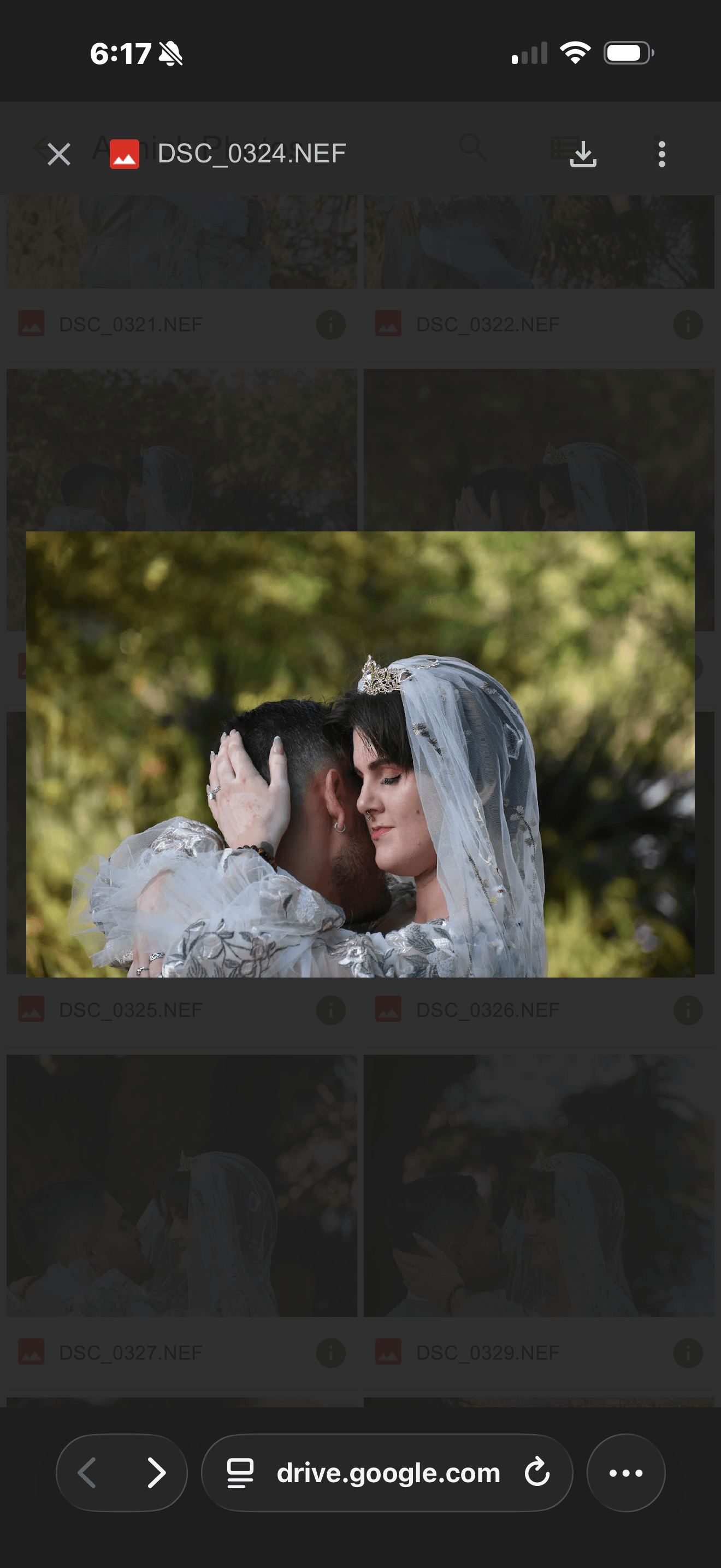 A bride and groom face each other outdoors, with trees in the background, embracing and smiling.