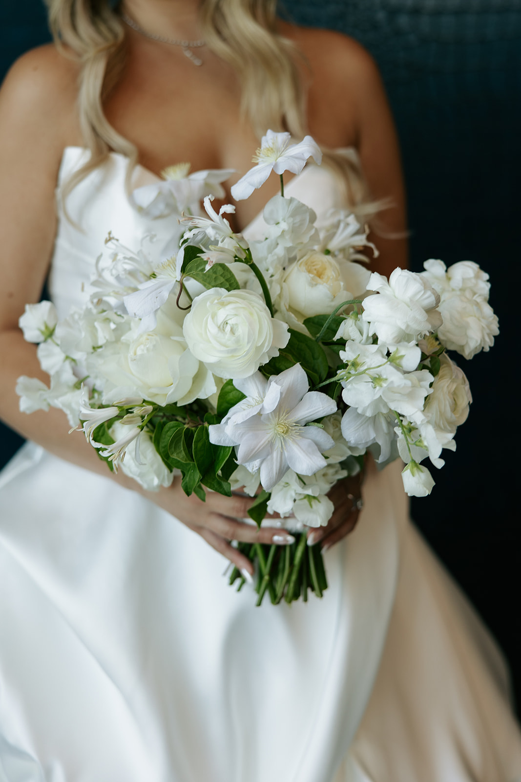 Person in white dress holding a bouquet of white flowers with green leaves, with blonde hair visible.