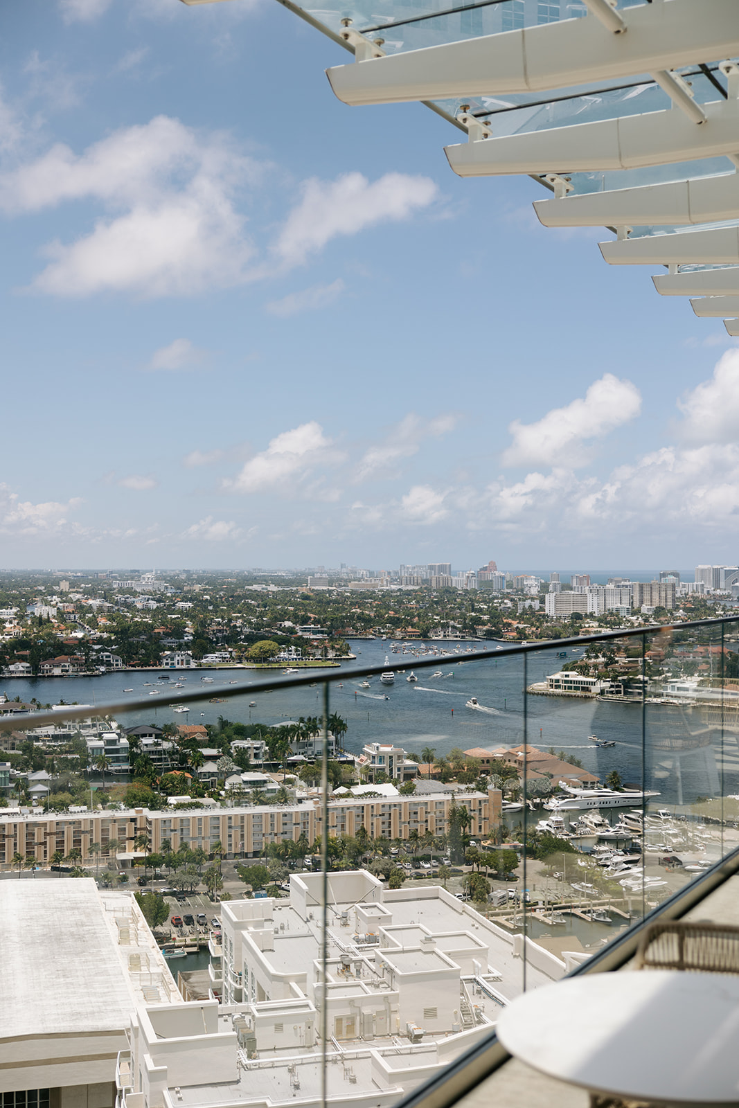 View of a cityscape with a river, buildings, and a partly cloudy sky, seen from a high vantage point with a glass railing.
