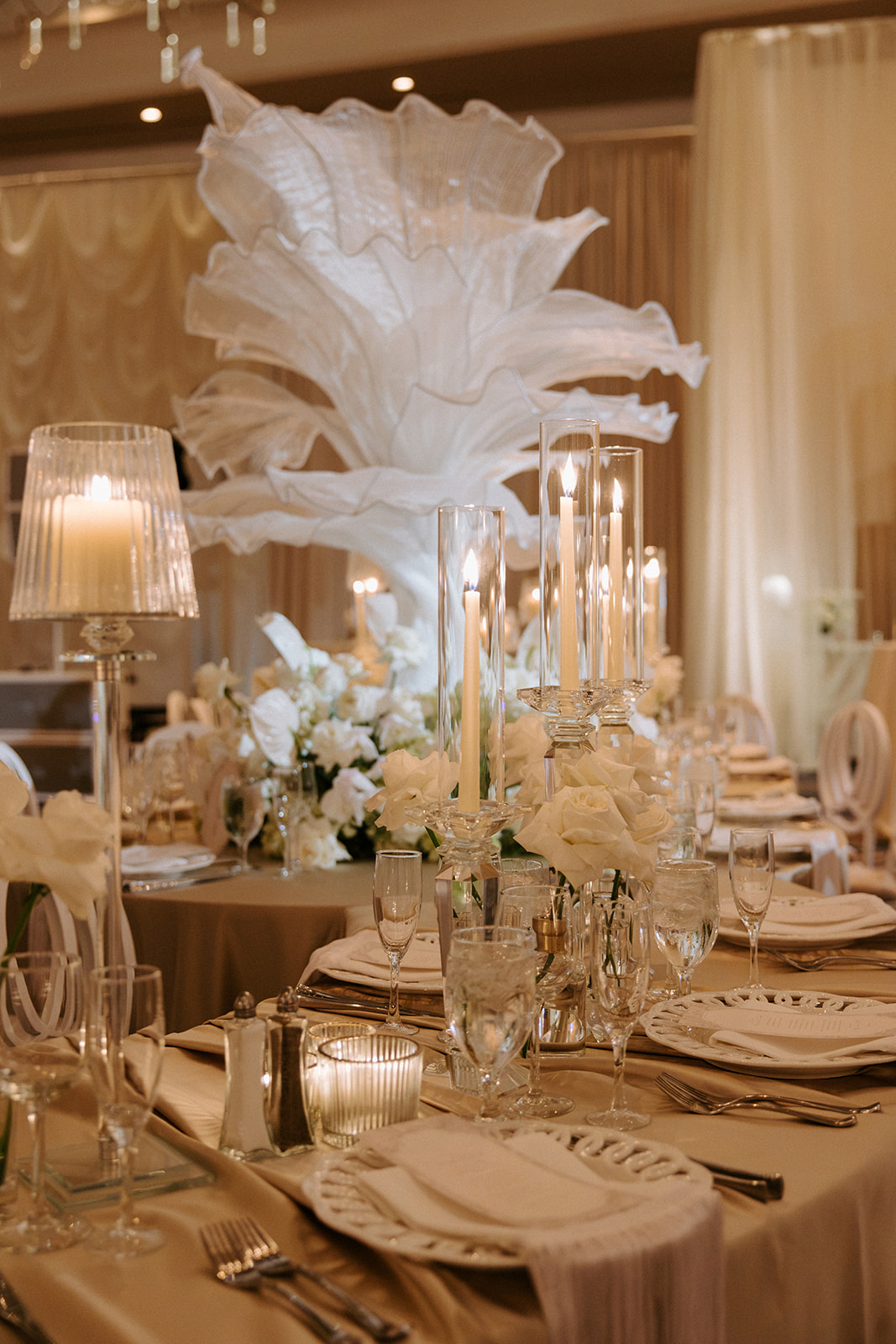 Elegant table setting with floral centerpiece, candles, and tableware in a warmly lit room.