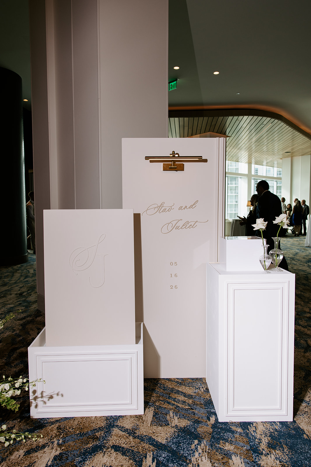 Display setup with white boards and stands in a modern indoor space, with people and large windows in the background.