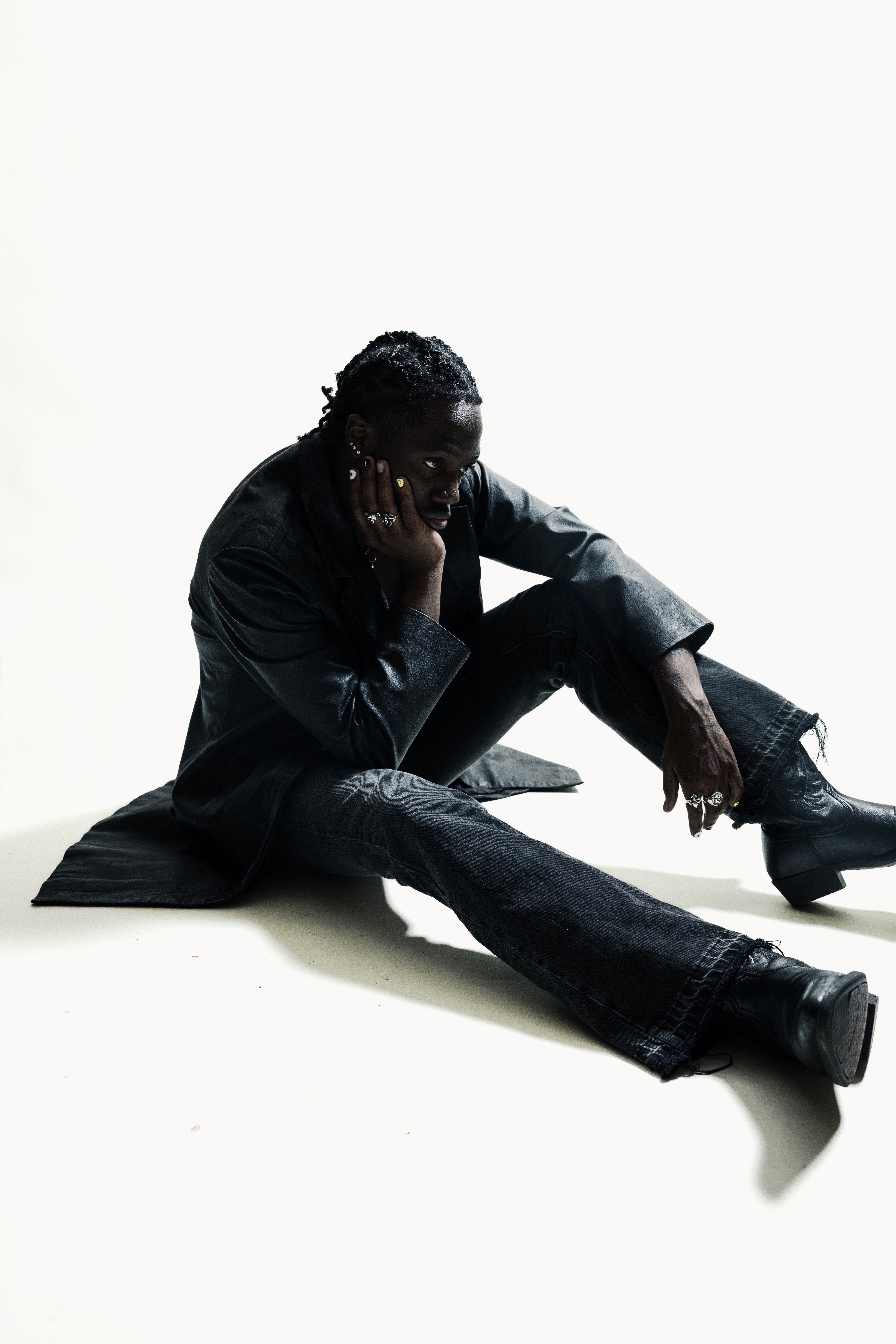 Person sitting on the floor with one hand on their face, wearing dark clothing, against a plain white background.
