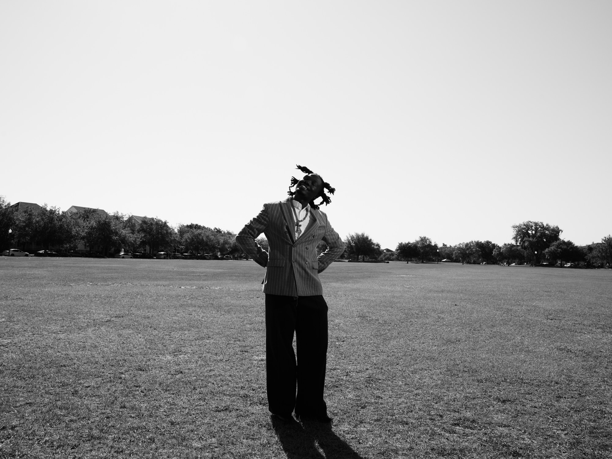 Person standing in an open field with hands on hips, trees in the background, black and white photo.