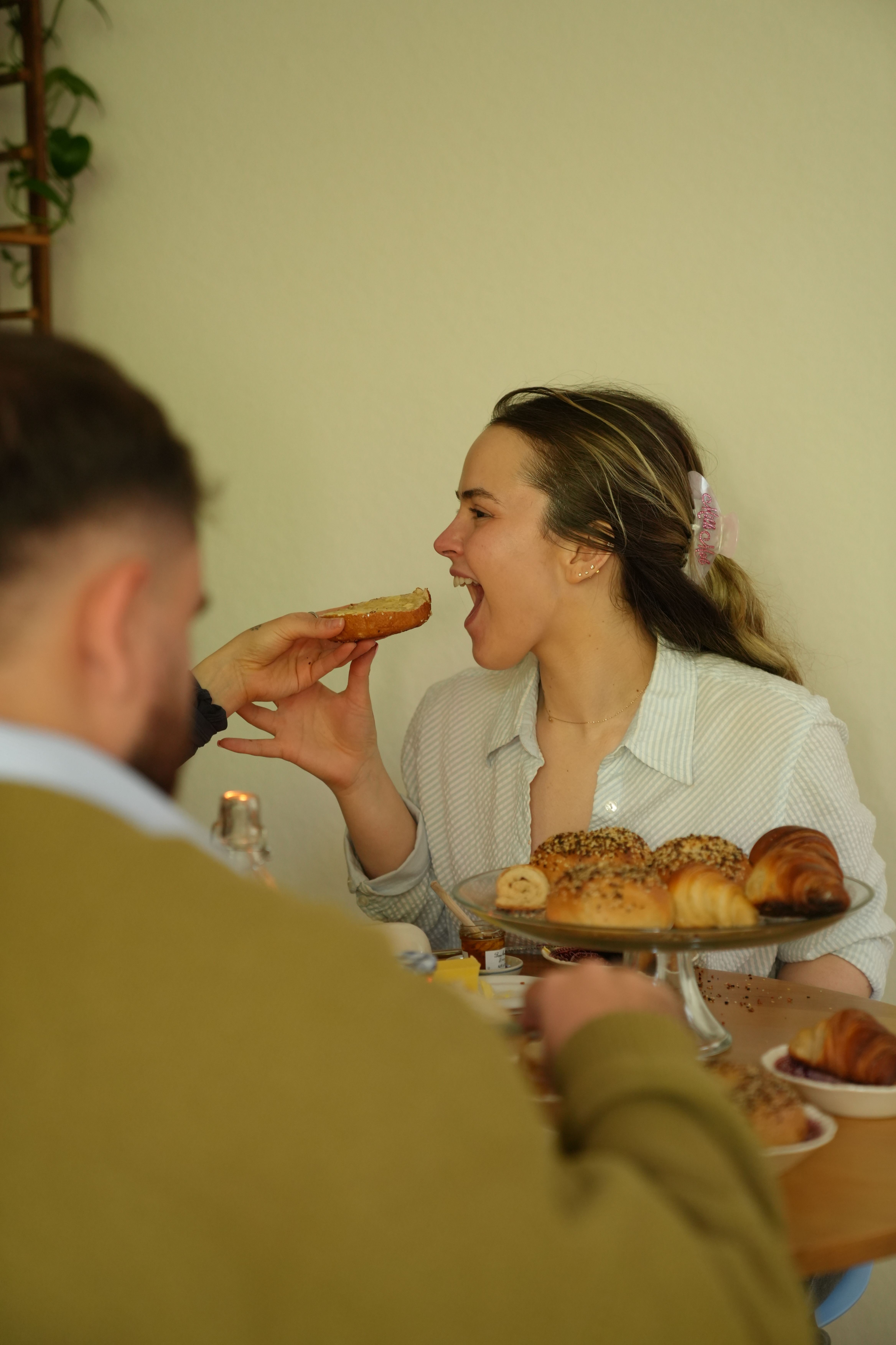 Person holding a slice of pizza near a woman sitting at a table with food, smiling and looking up.