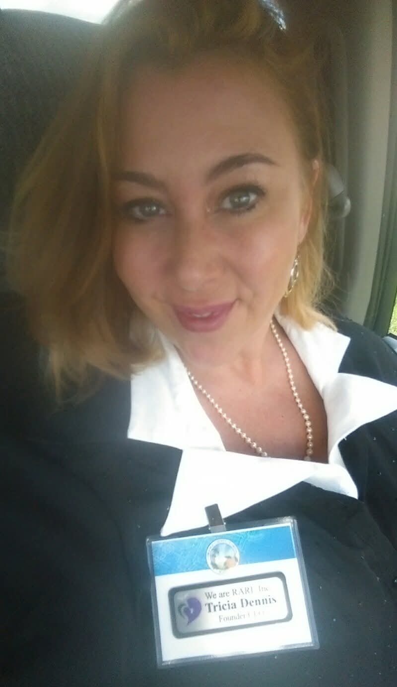 Woman with light brown hair, wearing a black and white striped top, and a name badge, smiling.