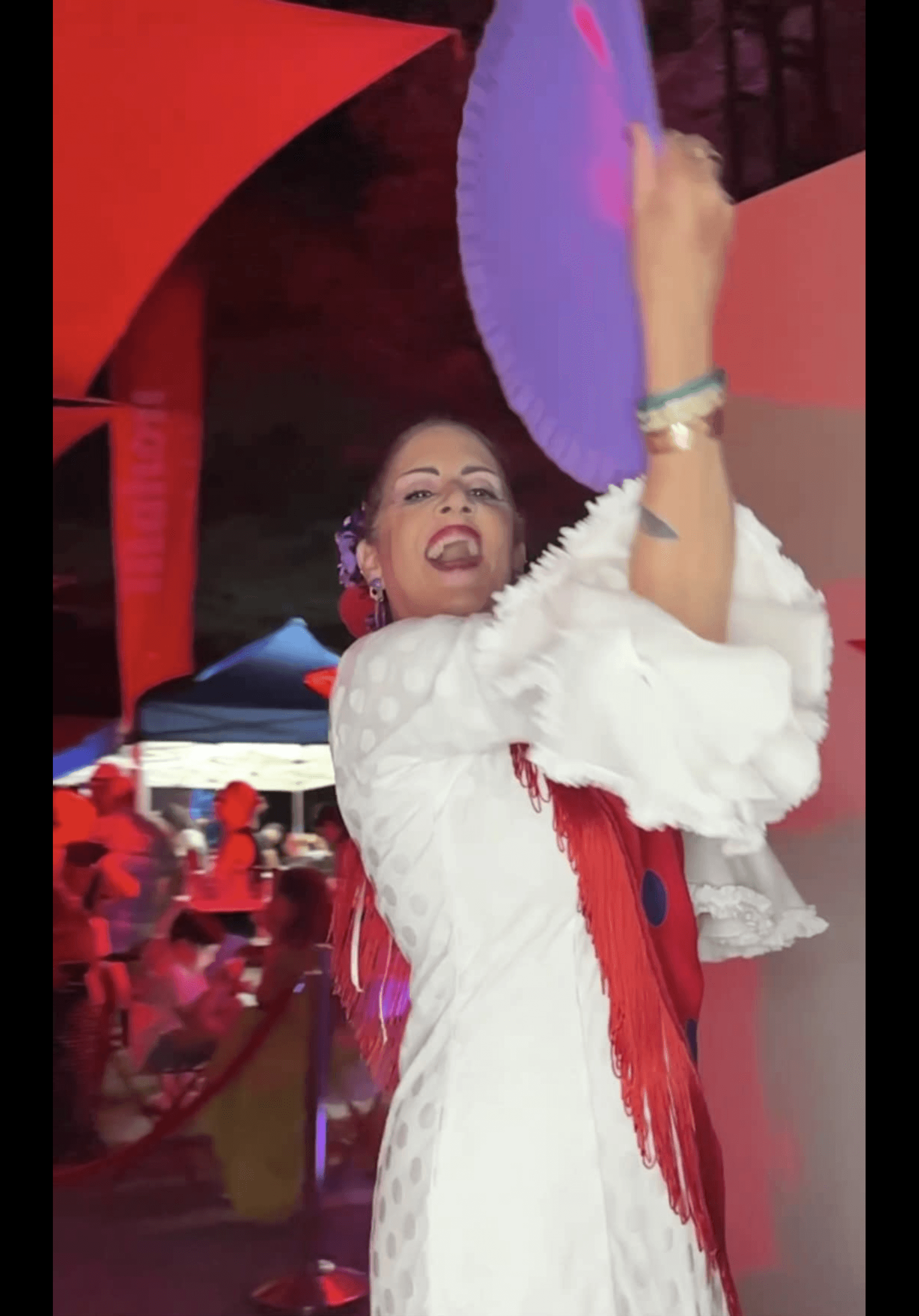Person holding a purple umbrella, smiling, wearing white and red clothing, with a lively background.