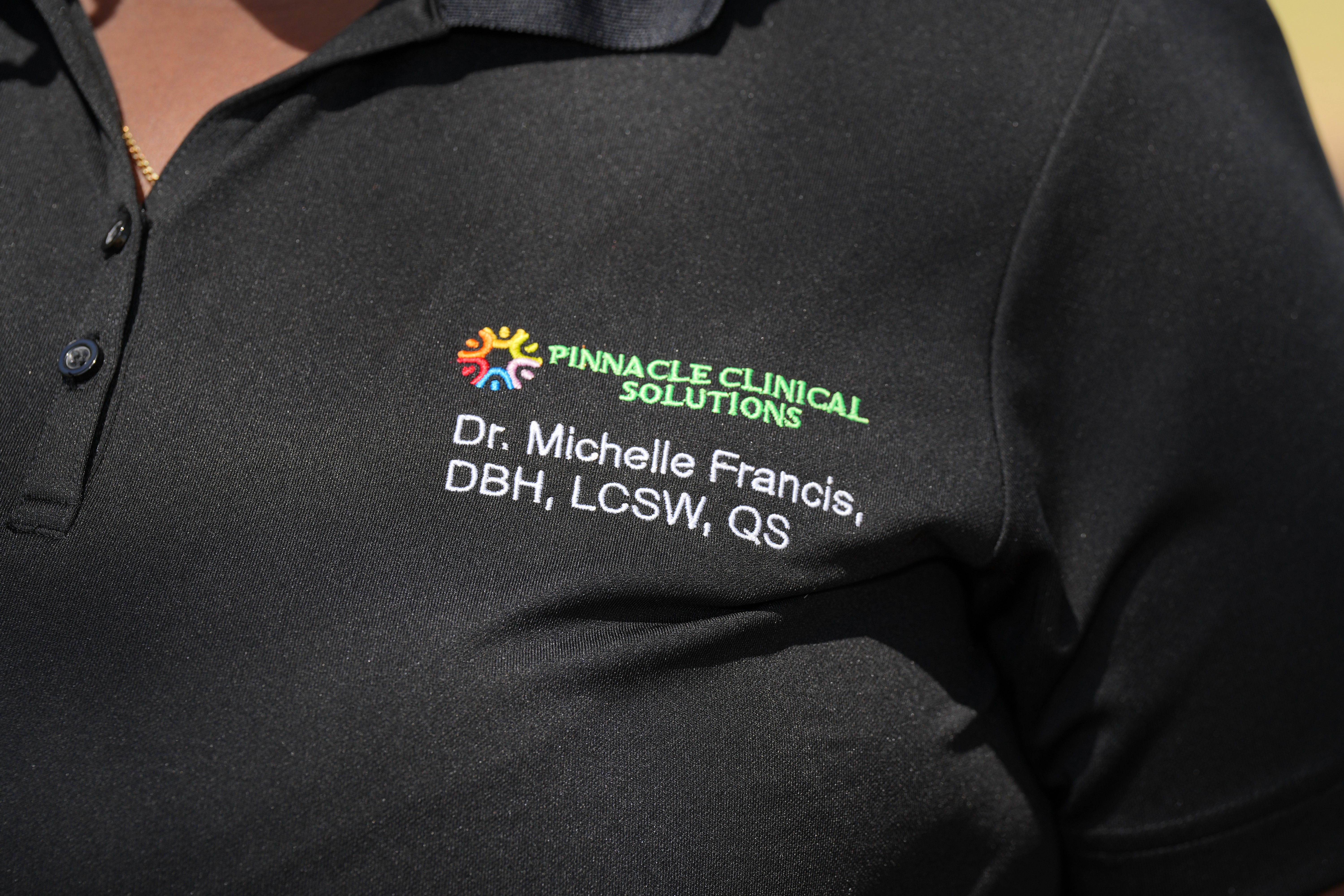 Close-up of a black uniform with Pinnacle Clinical Solutions logo and text, including a name and credentials.