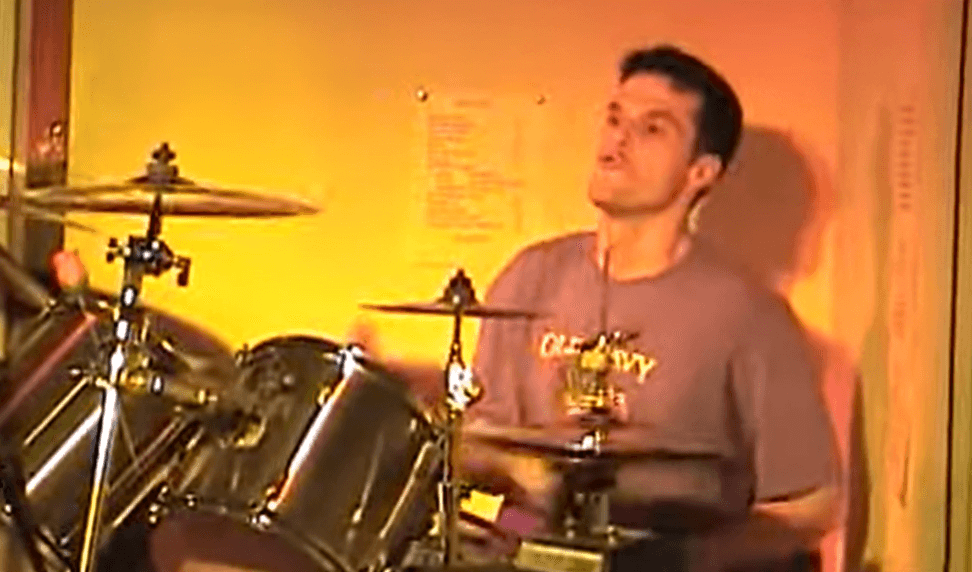 Young man playing drums in a room with yellow lighting, focused on his performance.