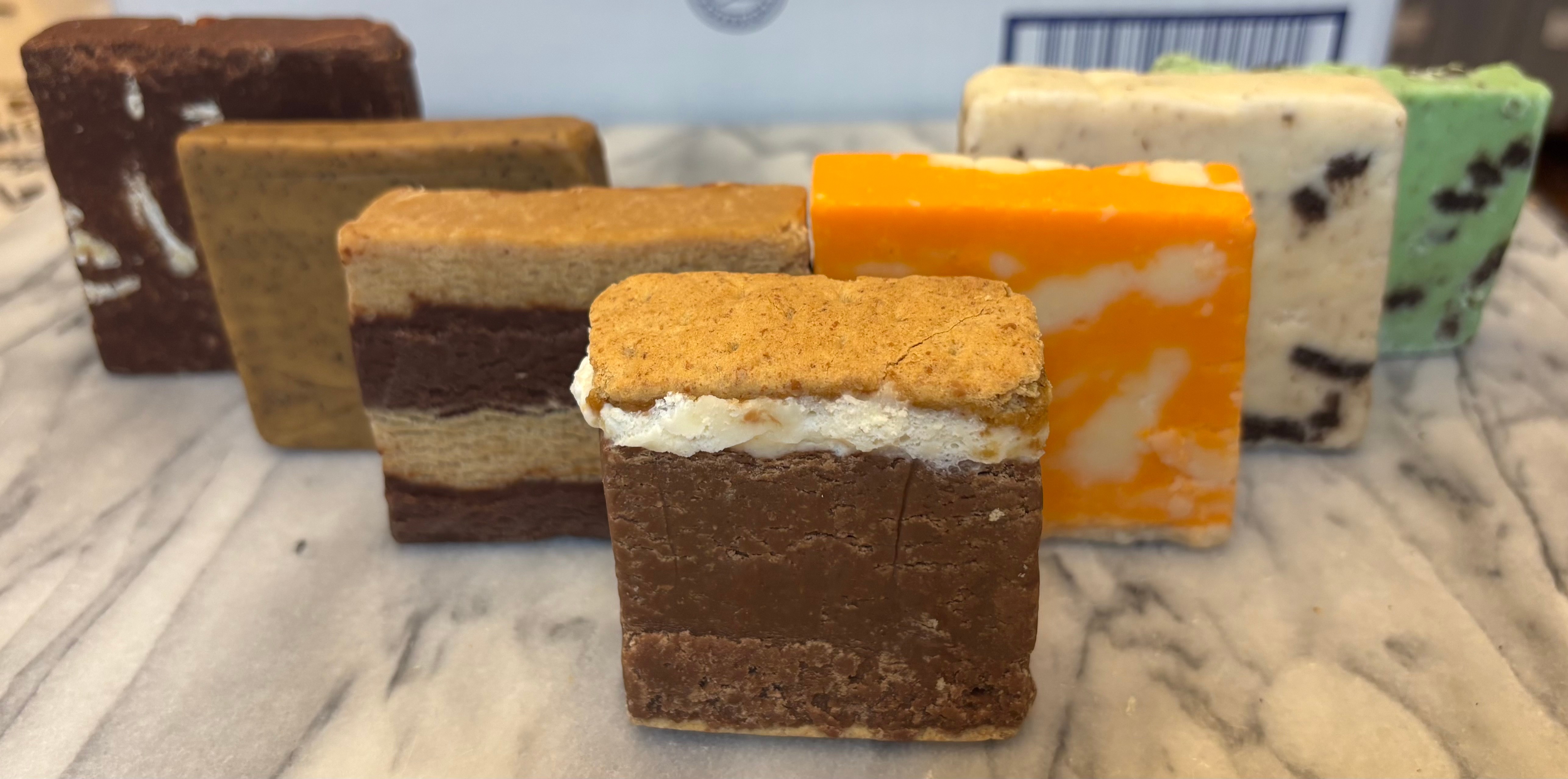 Assorted layered cookies with different flavors and colors on a marble surface.