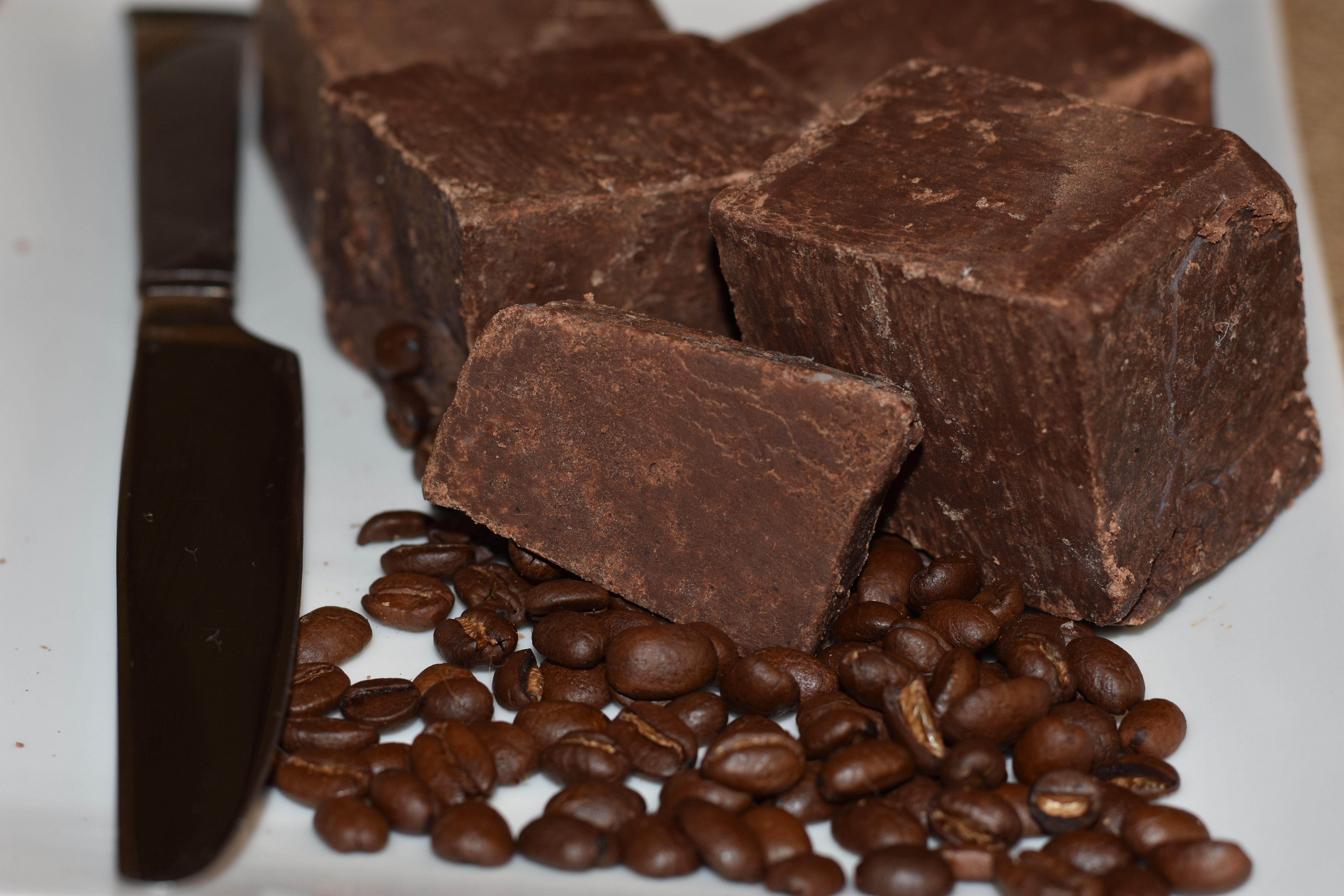 Large chunks of dark chocolate with coffee beans on a white plate, a knife on the side.