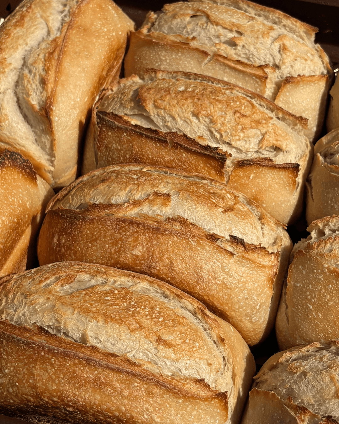 Close-up of sliced bread rolls with a golden crust and soft interior, arranged in a pile.