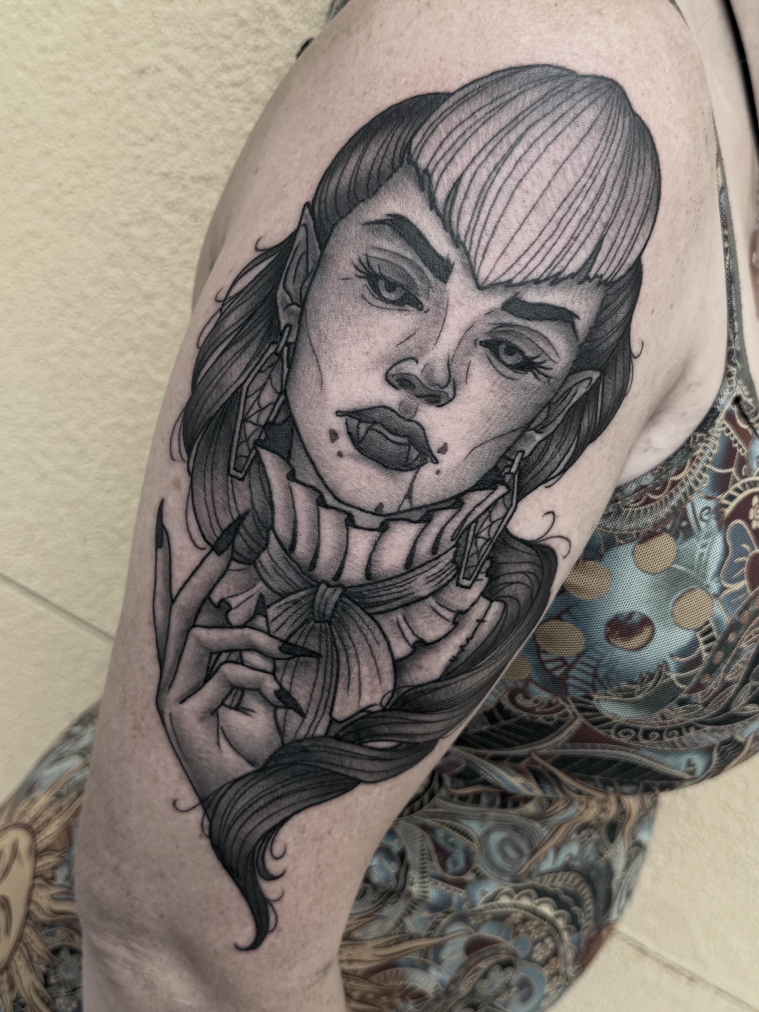 Black and gray tattoo of a woman's face with styled hair, makeup, and detailed shading on upper arm.