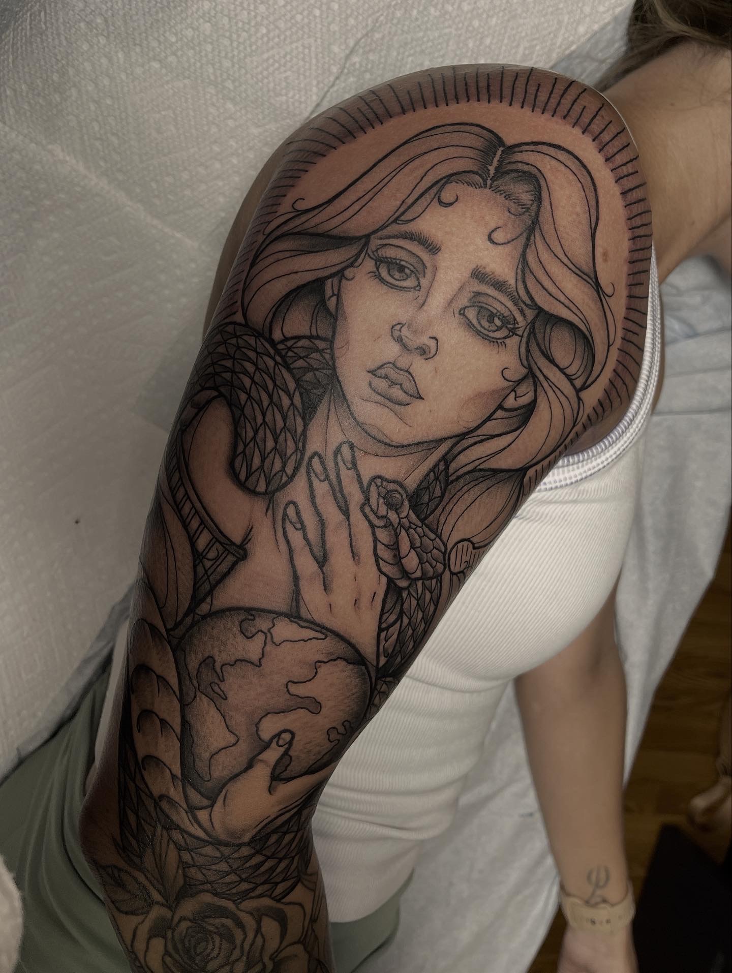 Tattoo of a woman with long hair, holding a snake, on person's upper arm, with detailed line work.