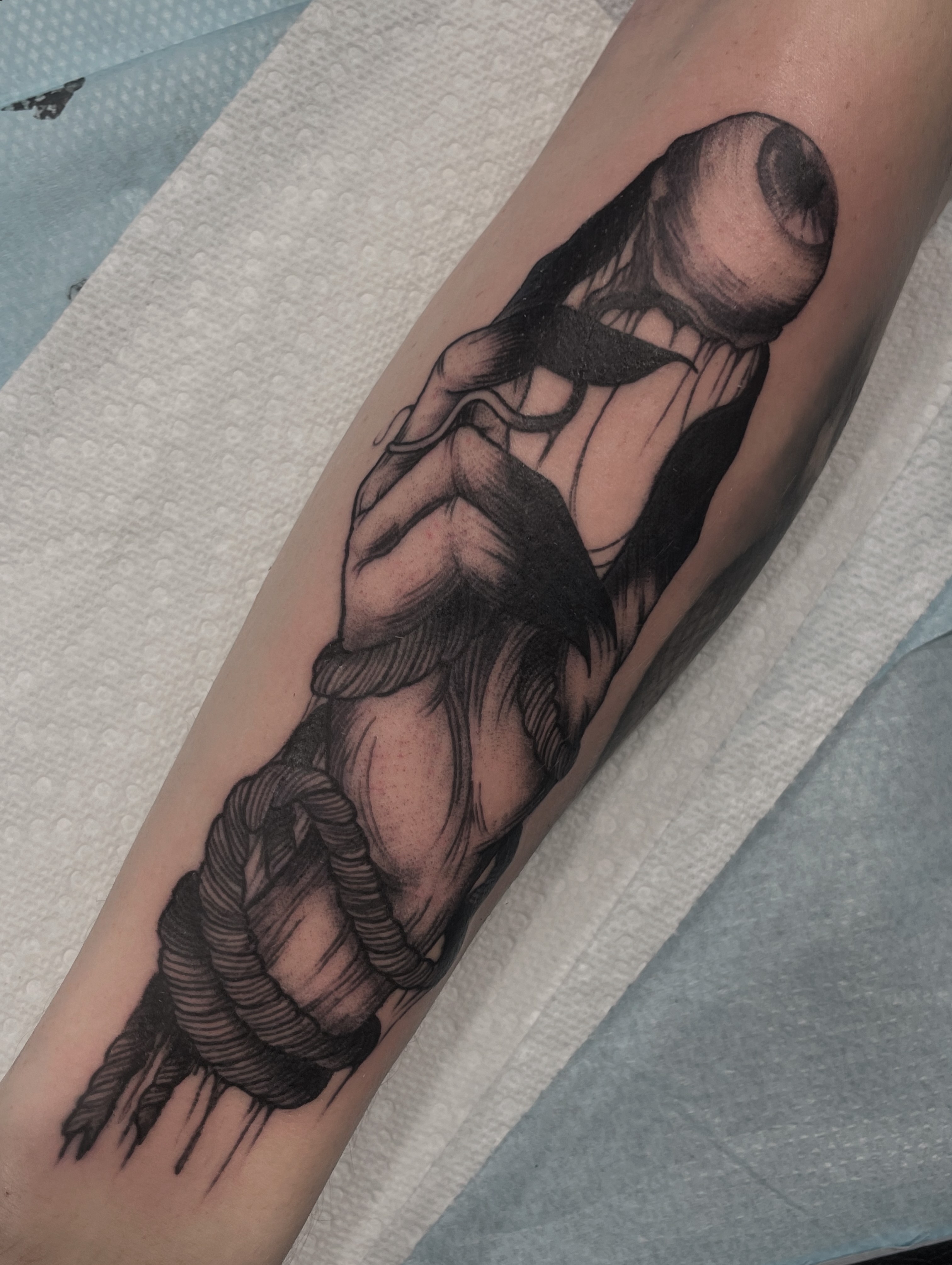 Black and gray tattoo of a woman with long hair, sitting with her knees drawn up, on a person's arm.