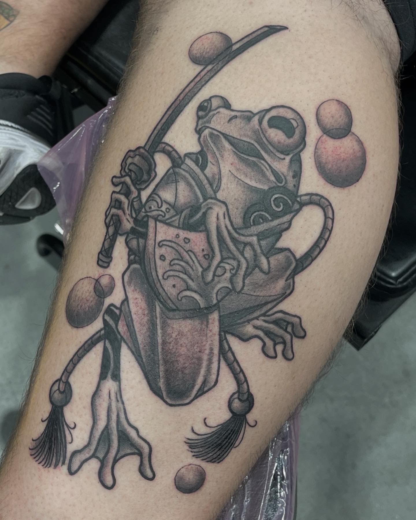Detailed frog with fishing rod sitting on a box, surrounded by floating spheres, in black and gray ink, realistic style.
