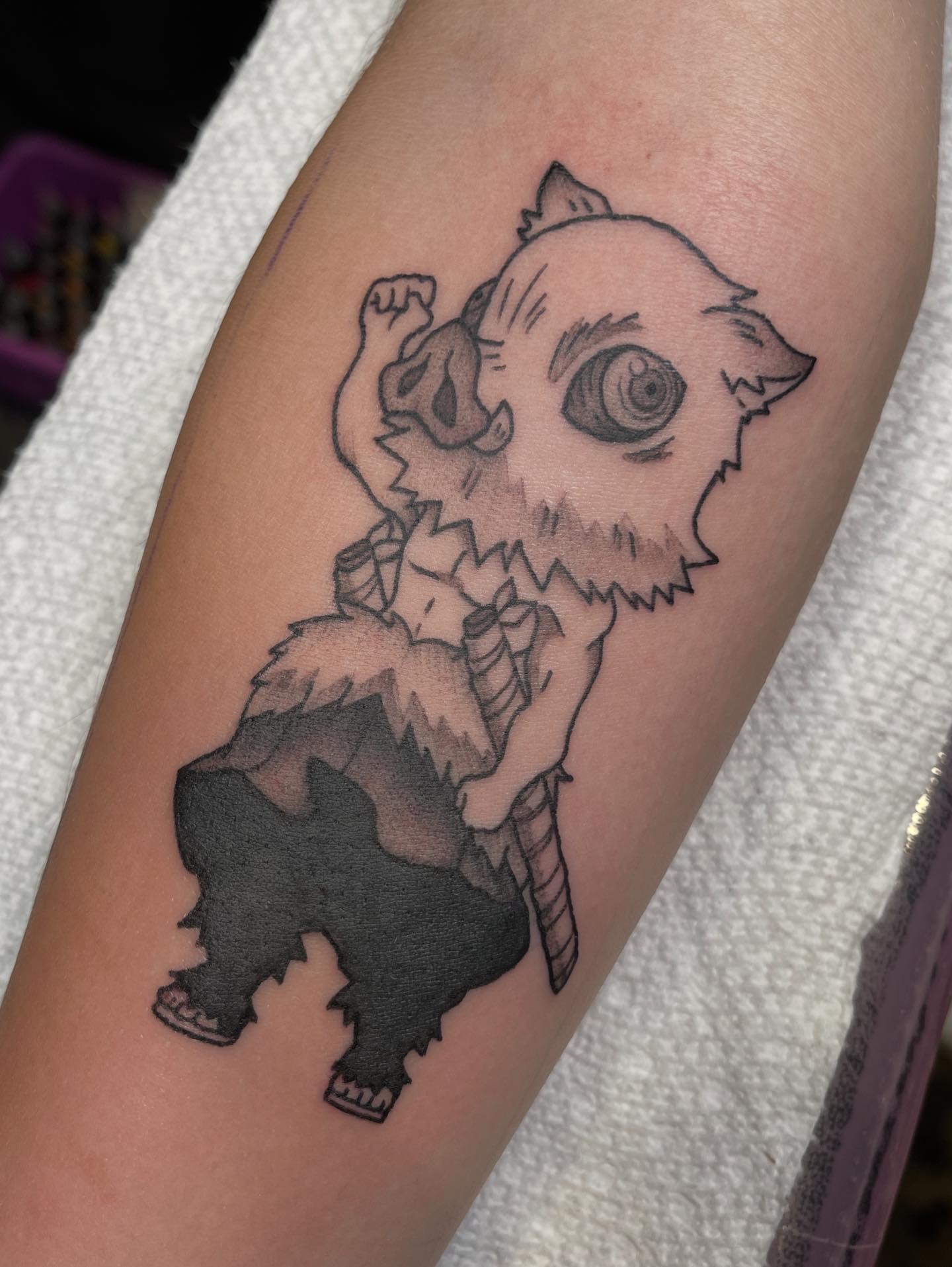 Tattoo of a small creature with a large eye, holding a sword, with a fluffy body and big paws.