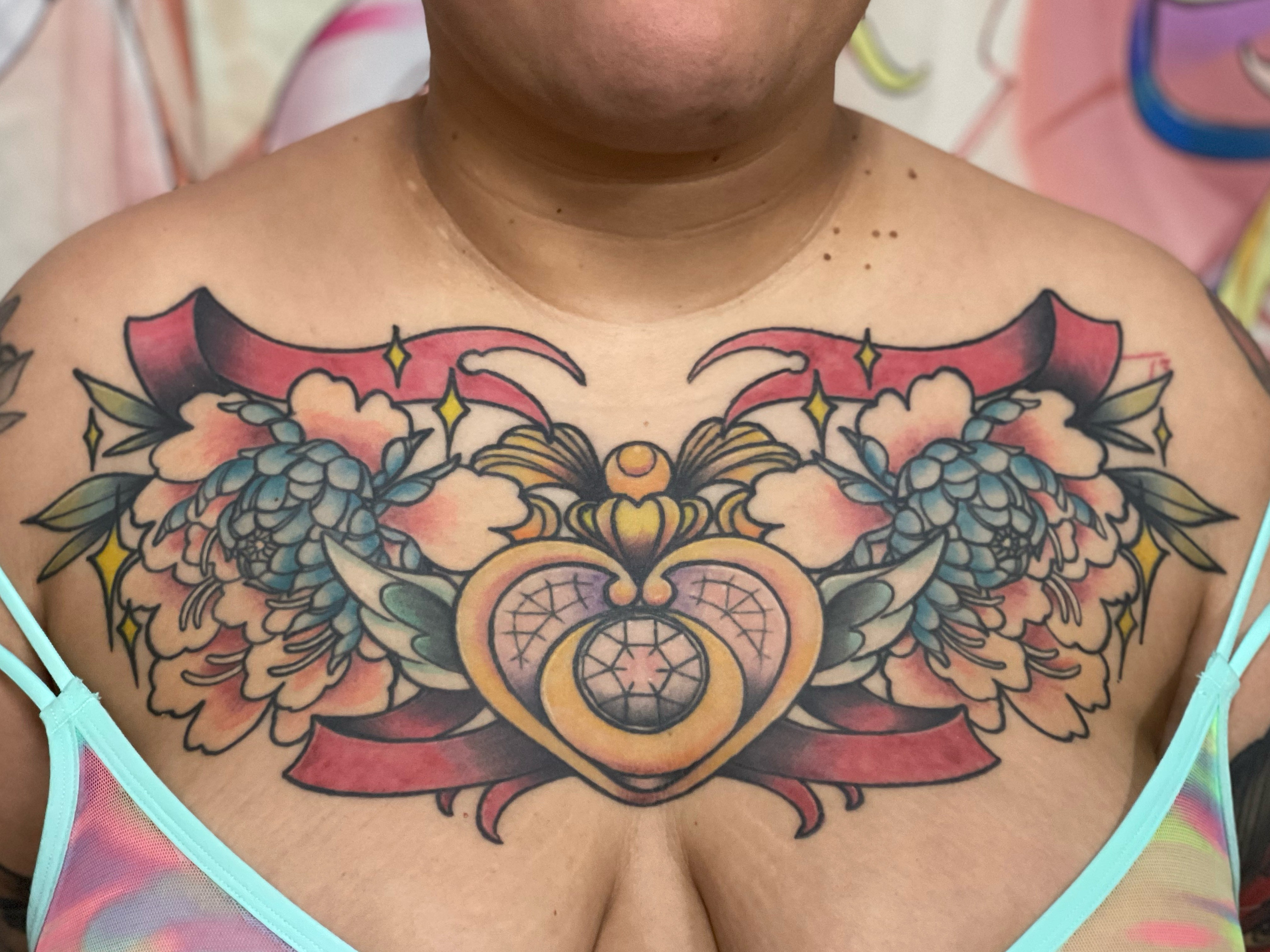 Colorful chest tattoo with hearts, ribbons, and floral elements across the upper chest.
