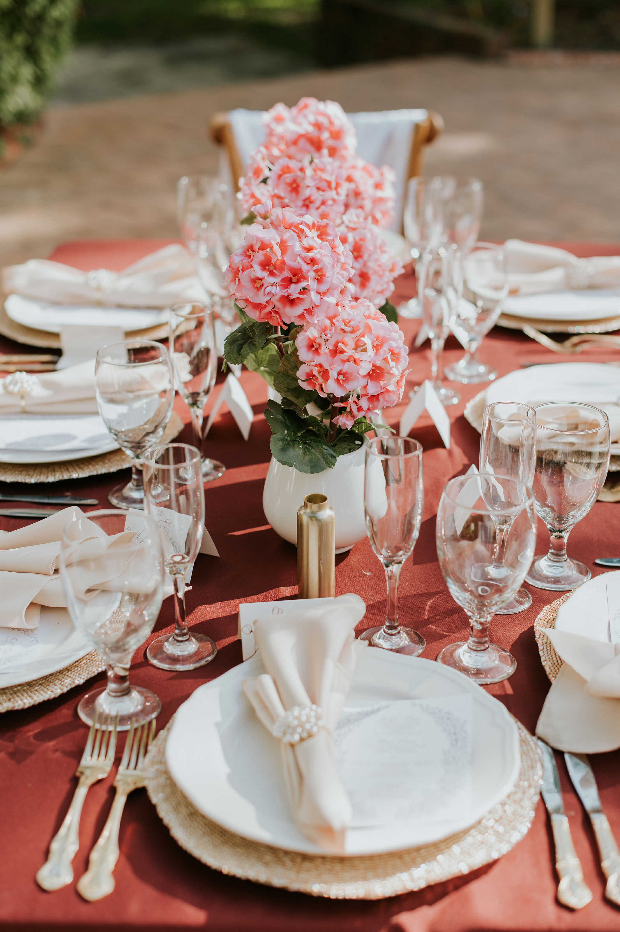 Table setting with a pink floral centerpiece, white plates, napkins, and glassware, arranged for a formal event.