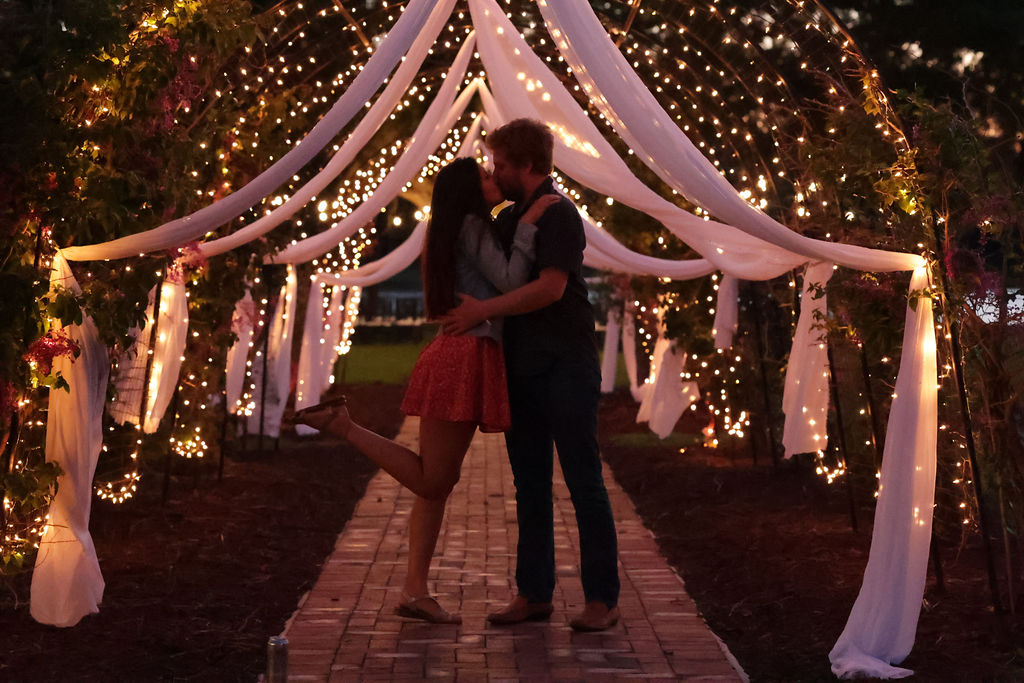 A couple kissing under a decorated canopy with string lights and flowing fabric at night.