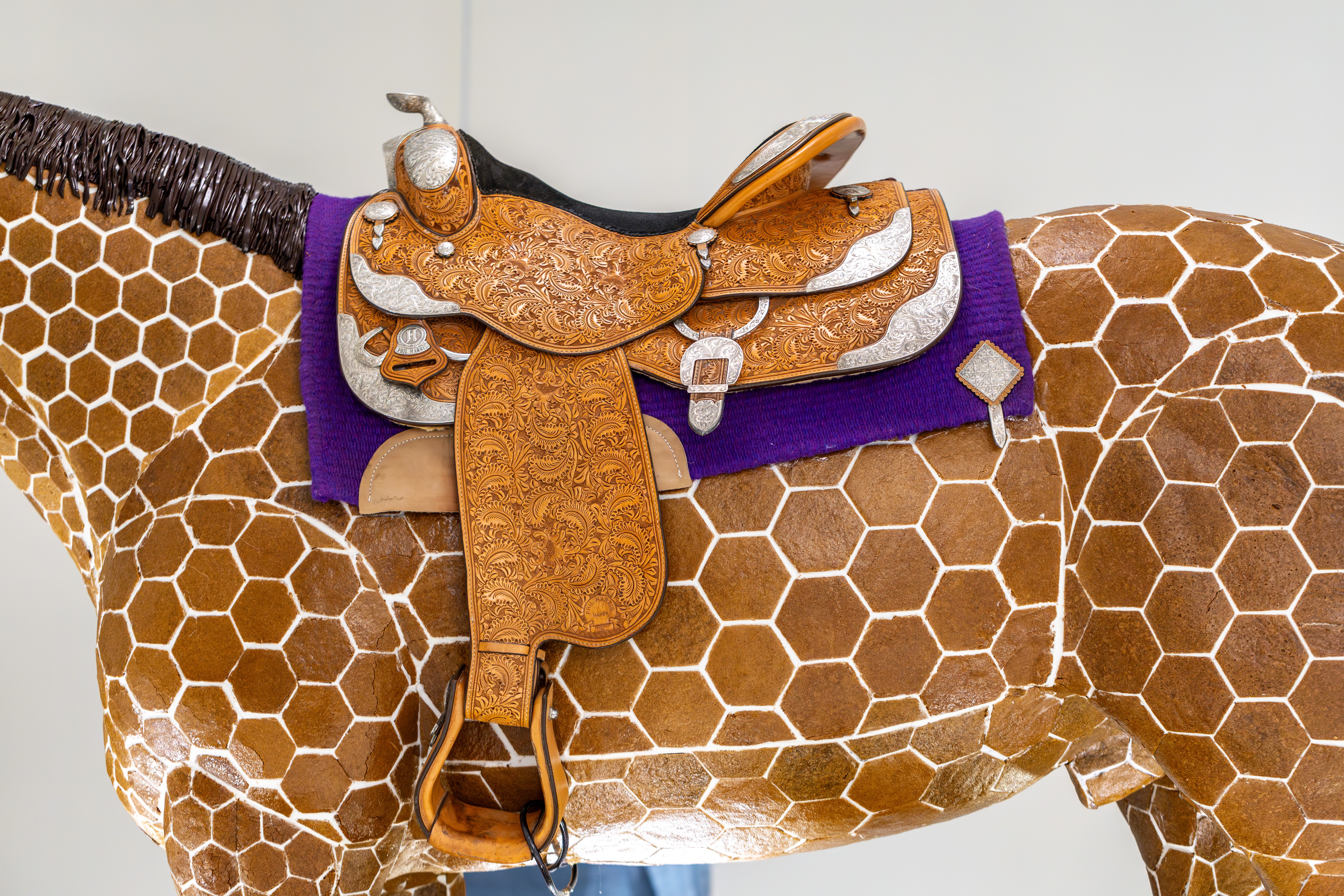 Close-up of a giraffe-shaped saddle with a decorative leather head and purple accents on a giraffe's back.