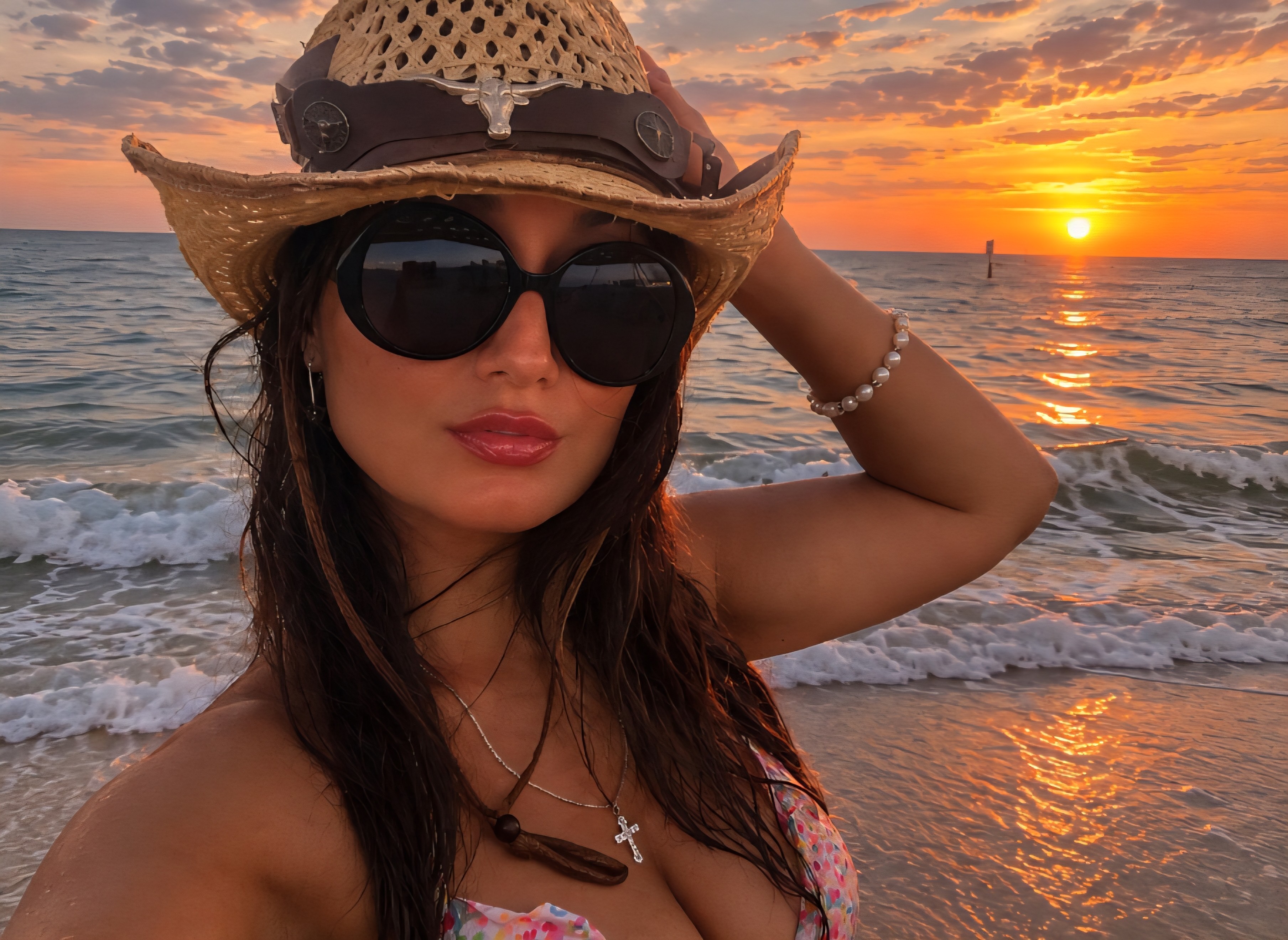 Woman wearing sunglasses and a hat on the beach during sunset, with ocean waves in the background.