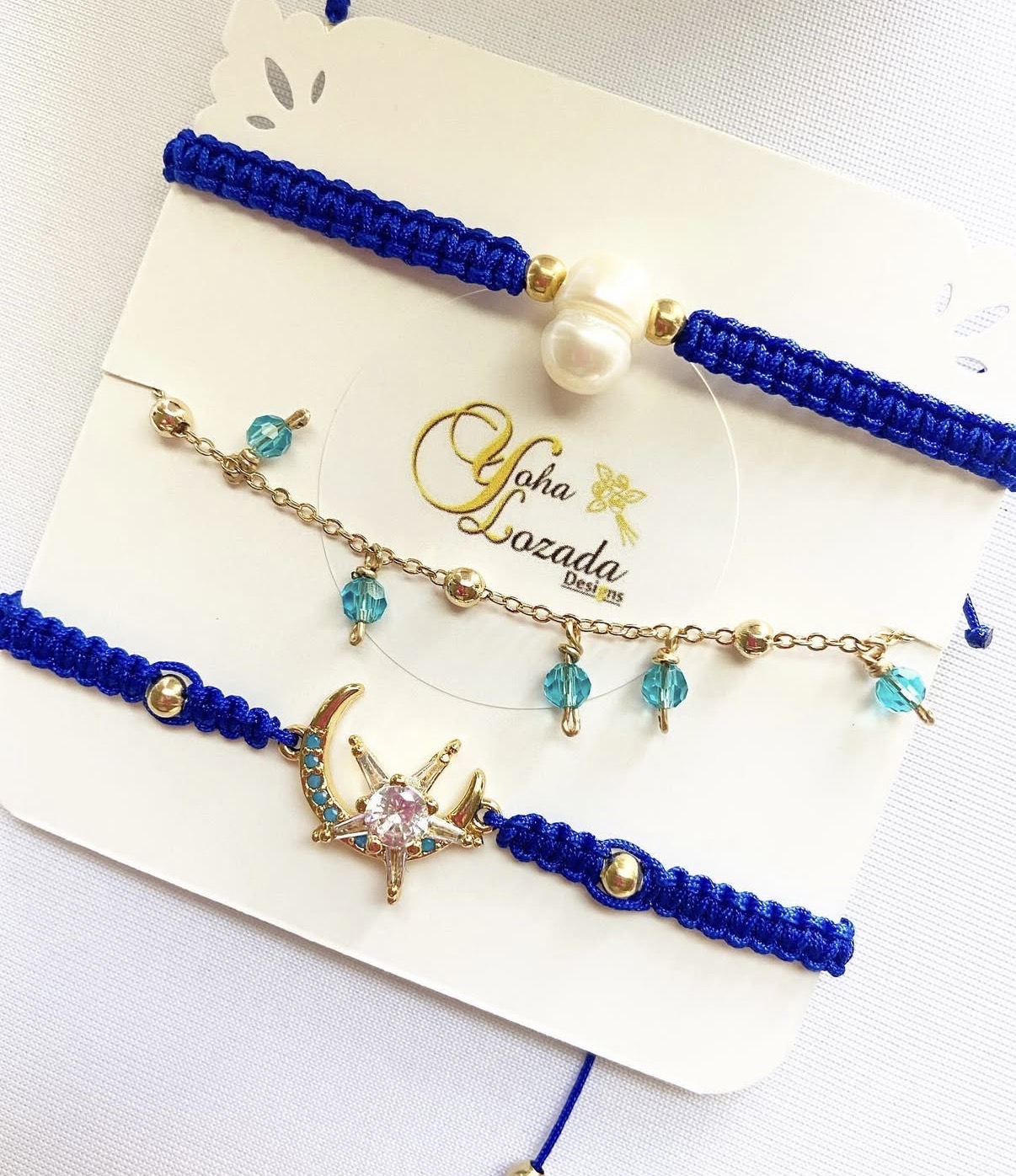 Set of three blue woven bracelets and a gold chain with a starfish charm and blue beads, displayed on a white card.