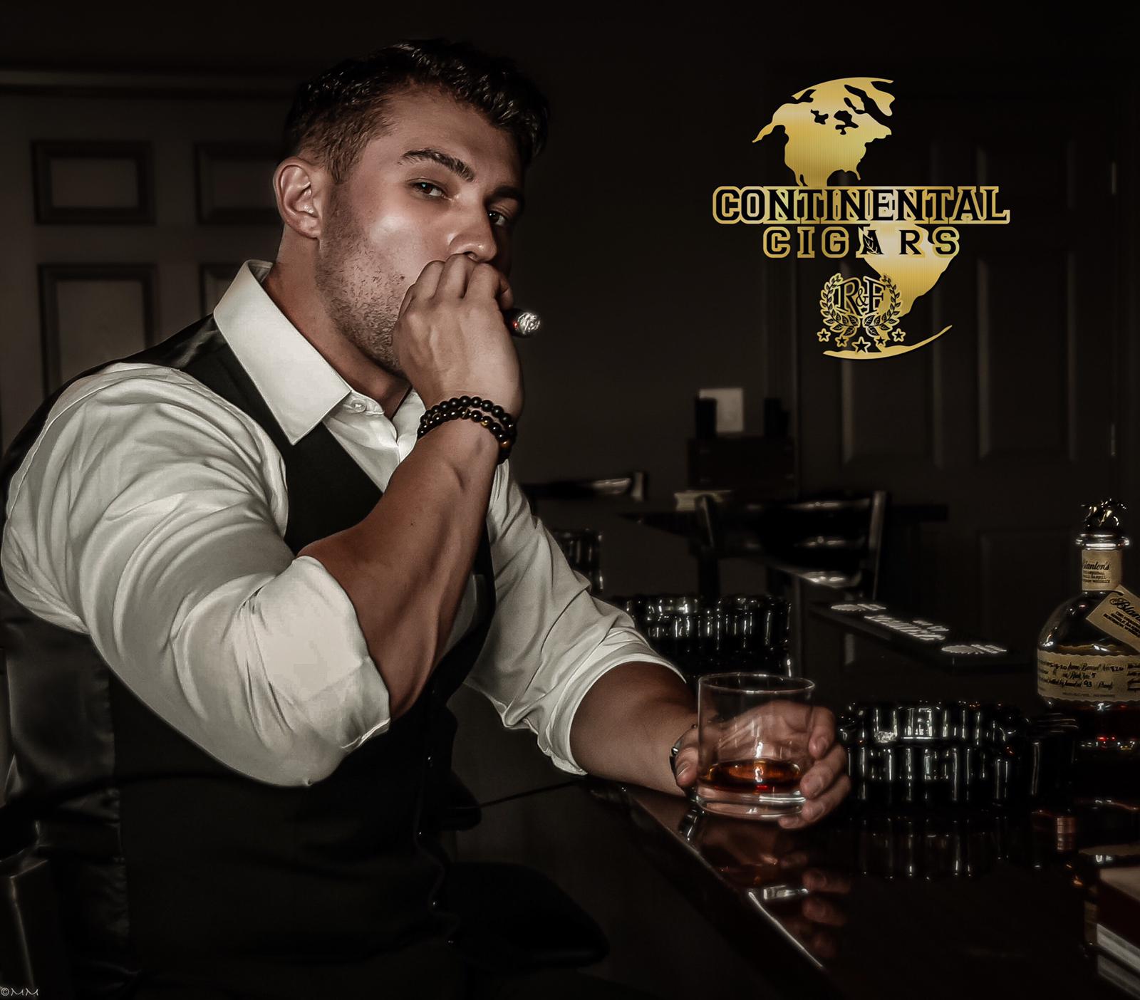 Man sitting at bar holding a glass, smoking, with a logo reading 'Continental Cigars' in the background.