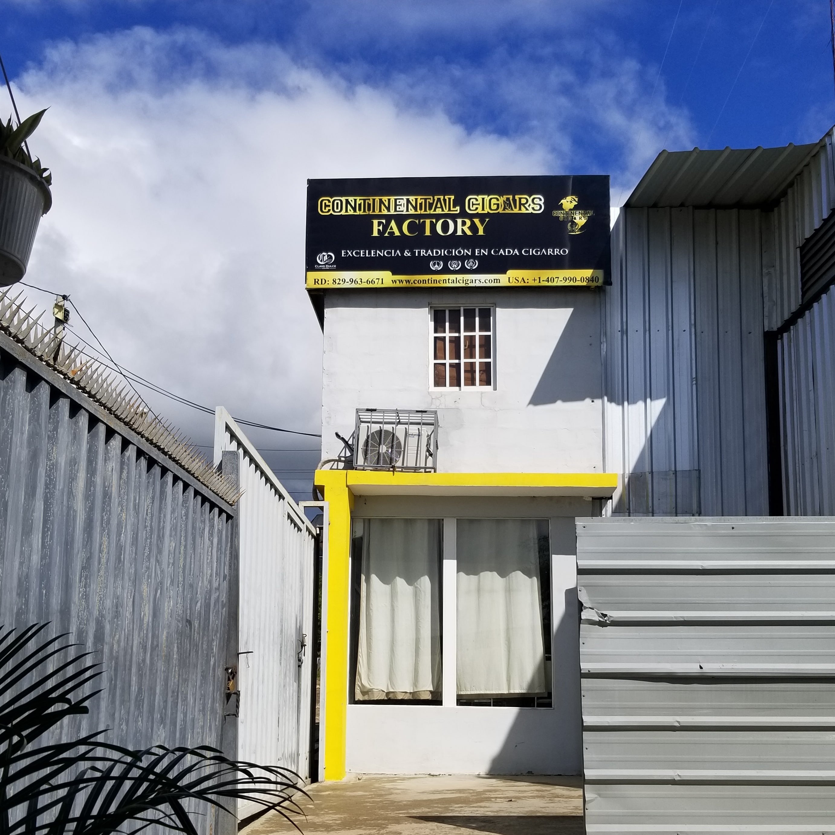 Building with a sign reading 'Conventual Cigars Factory' and a yellow stripe, under a partly cloudy sky.