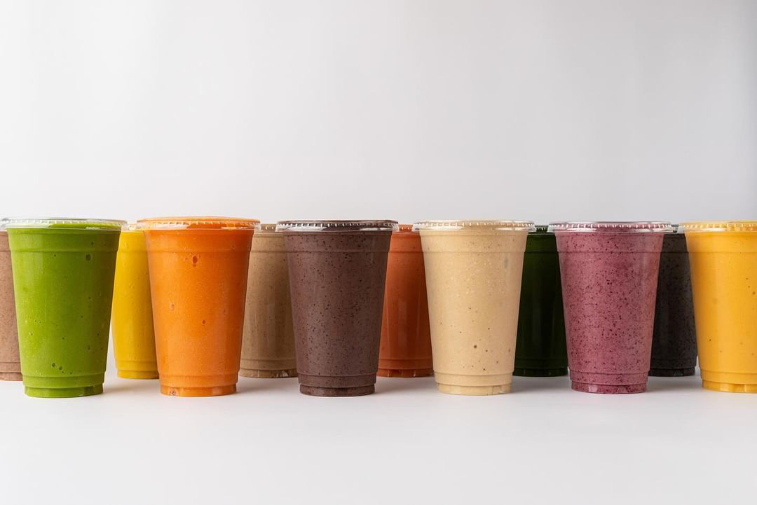 Row of colorful cups with various shades including green, orange, brown, beige, pink, and yellow, on a white surface.