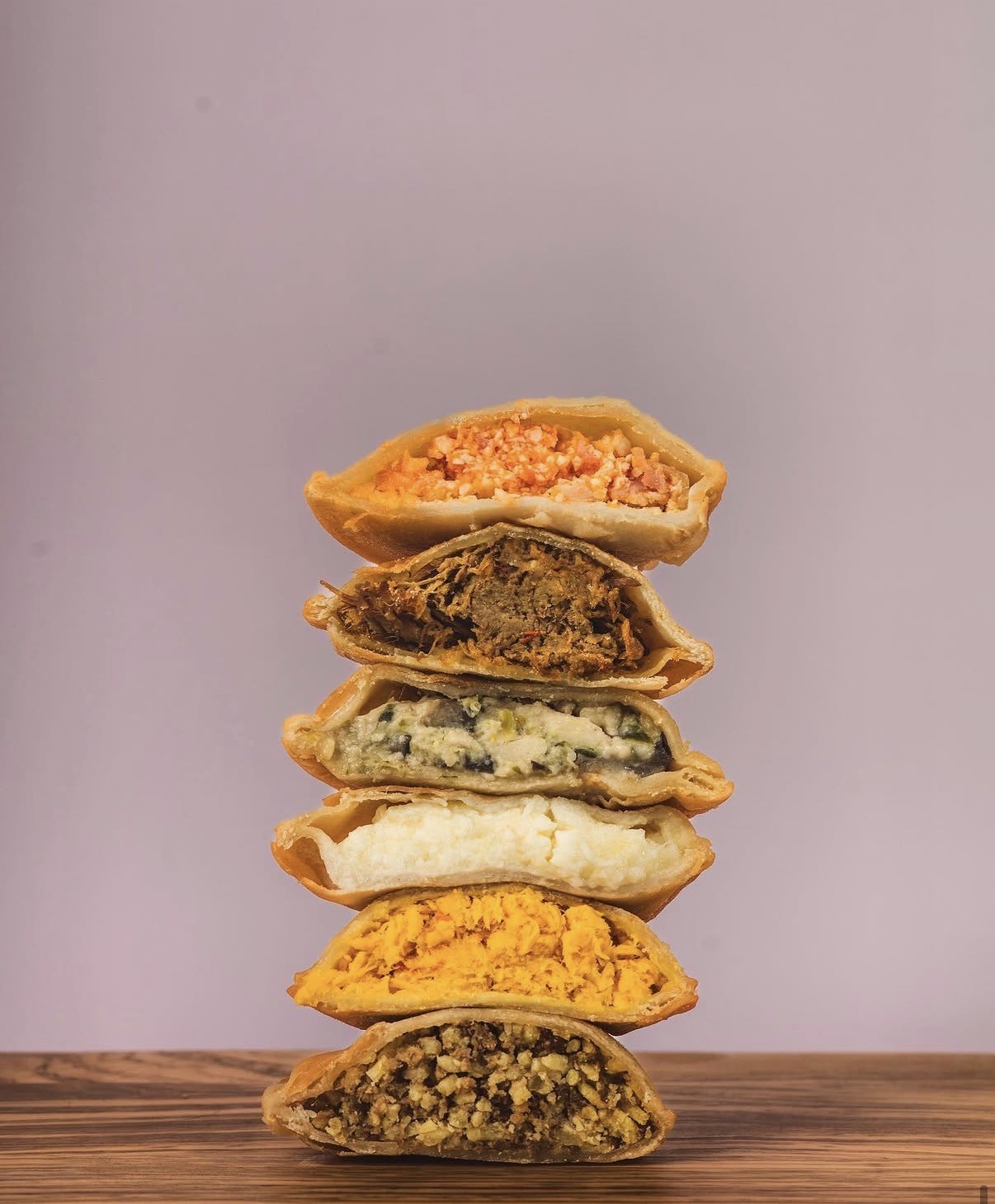 Stack of six assorted stuffed pastries on a wooden surface against a plain background.