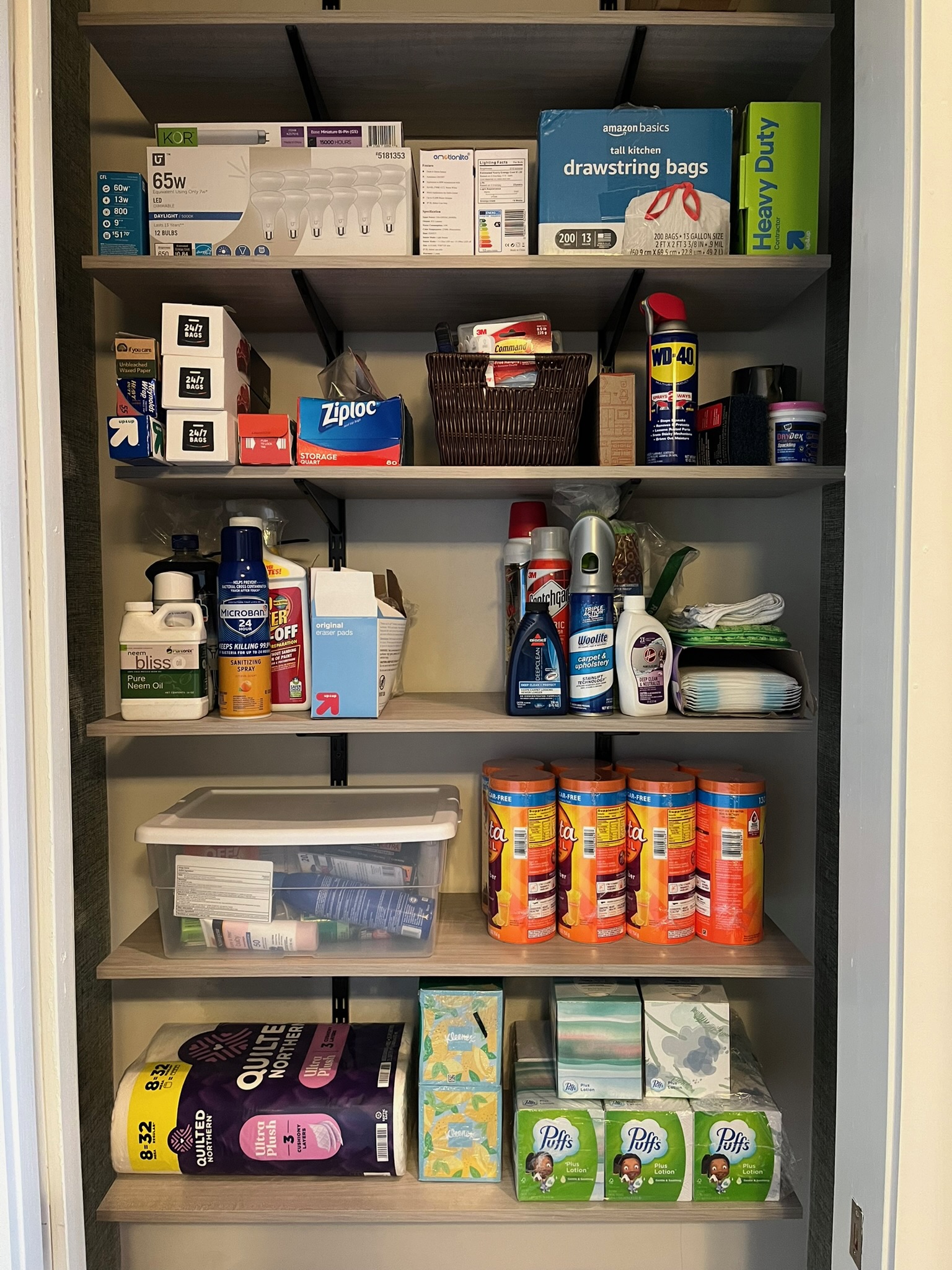 Shelves filled with household supplies including trash bags, cleaning products, paper towels, and canned goods.