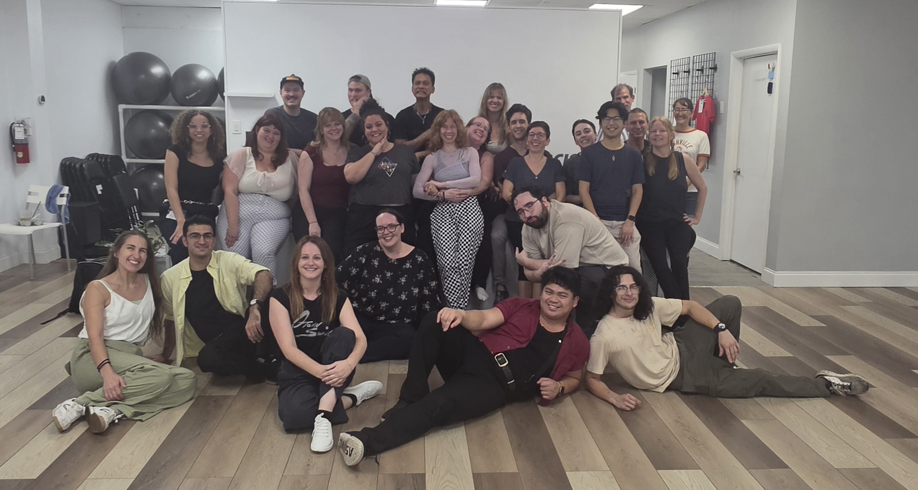 Group of people in a room, some sitting on the floor, others standing, posing for a photo.