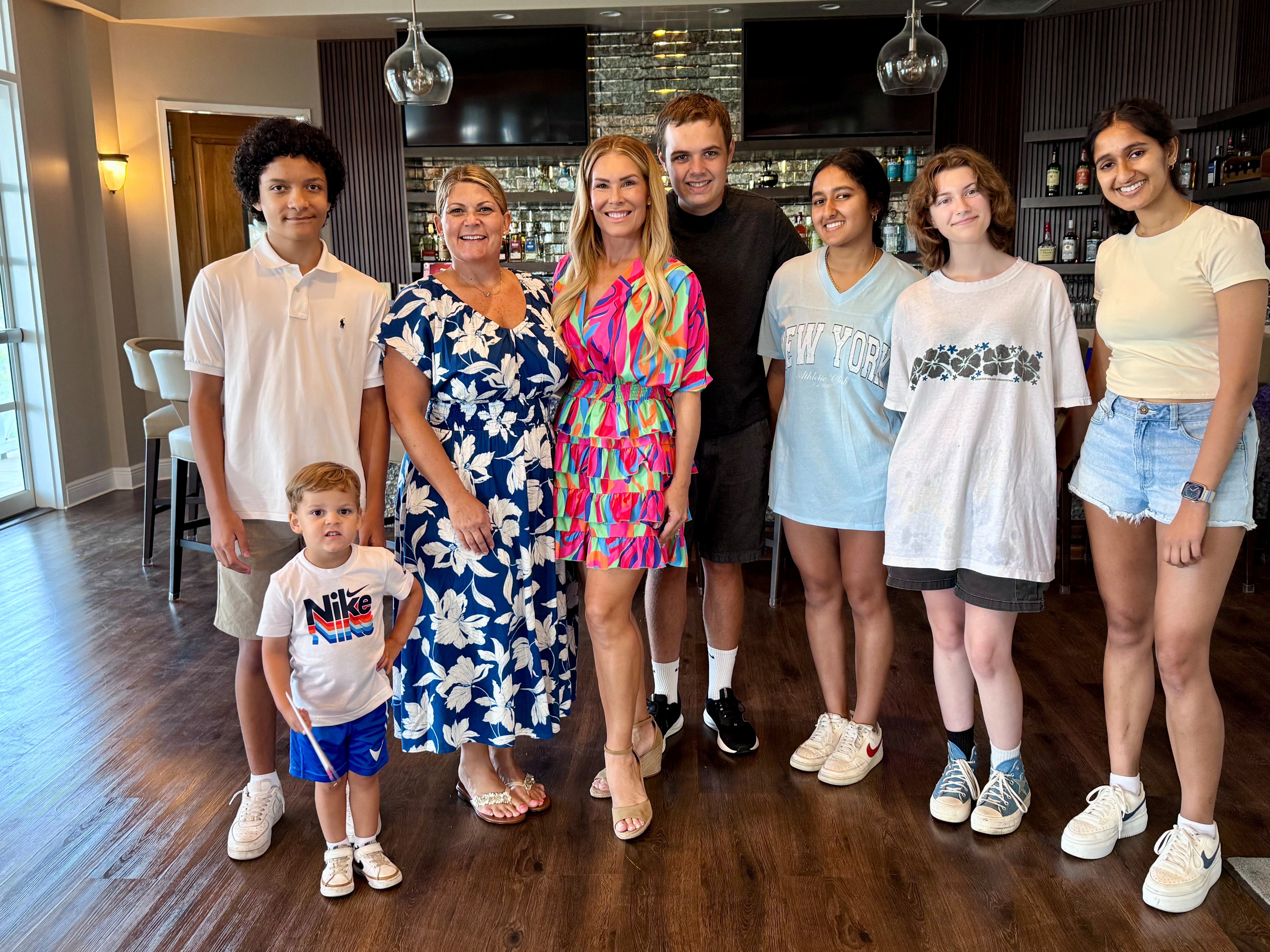 Group of eight people, including children, standing indoors in a modern kitchen, smiling at the camera.