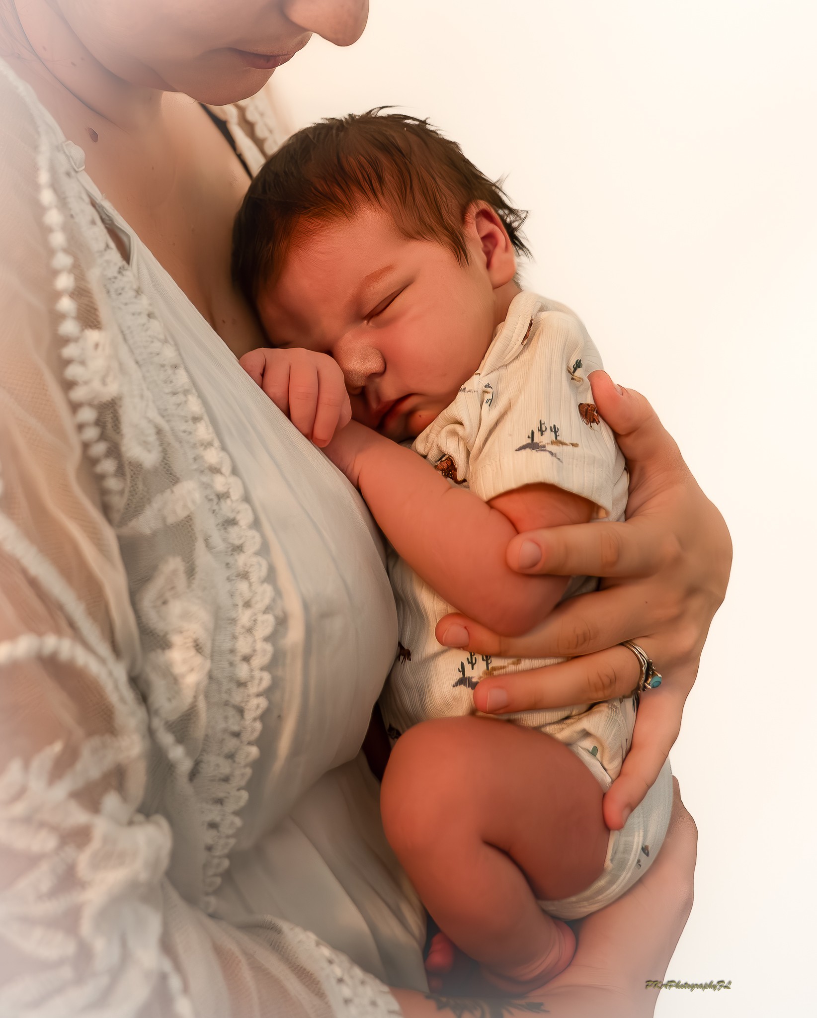 Person holding a sleeping baby close, with the baby's face resting on their chest, in a light-colored top.