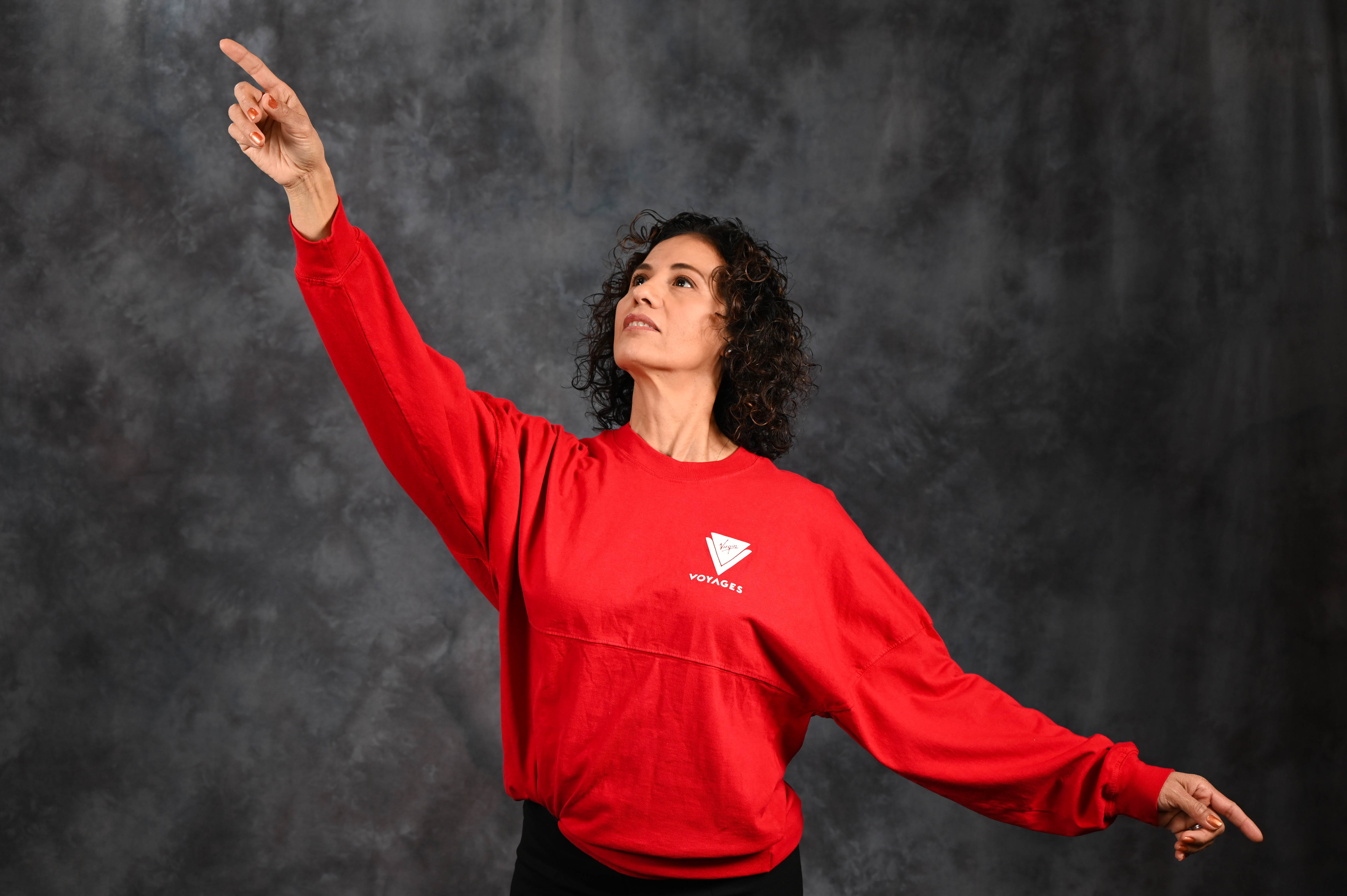 Woman in red sweatshirt pointing upward with dark background.