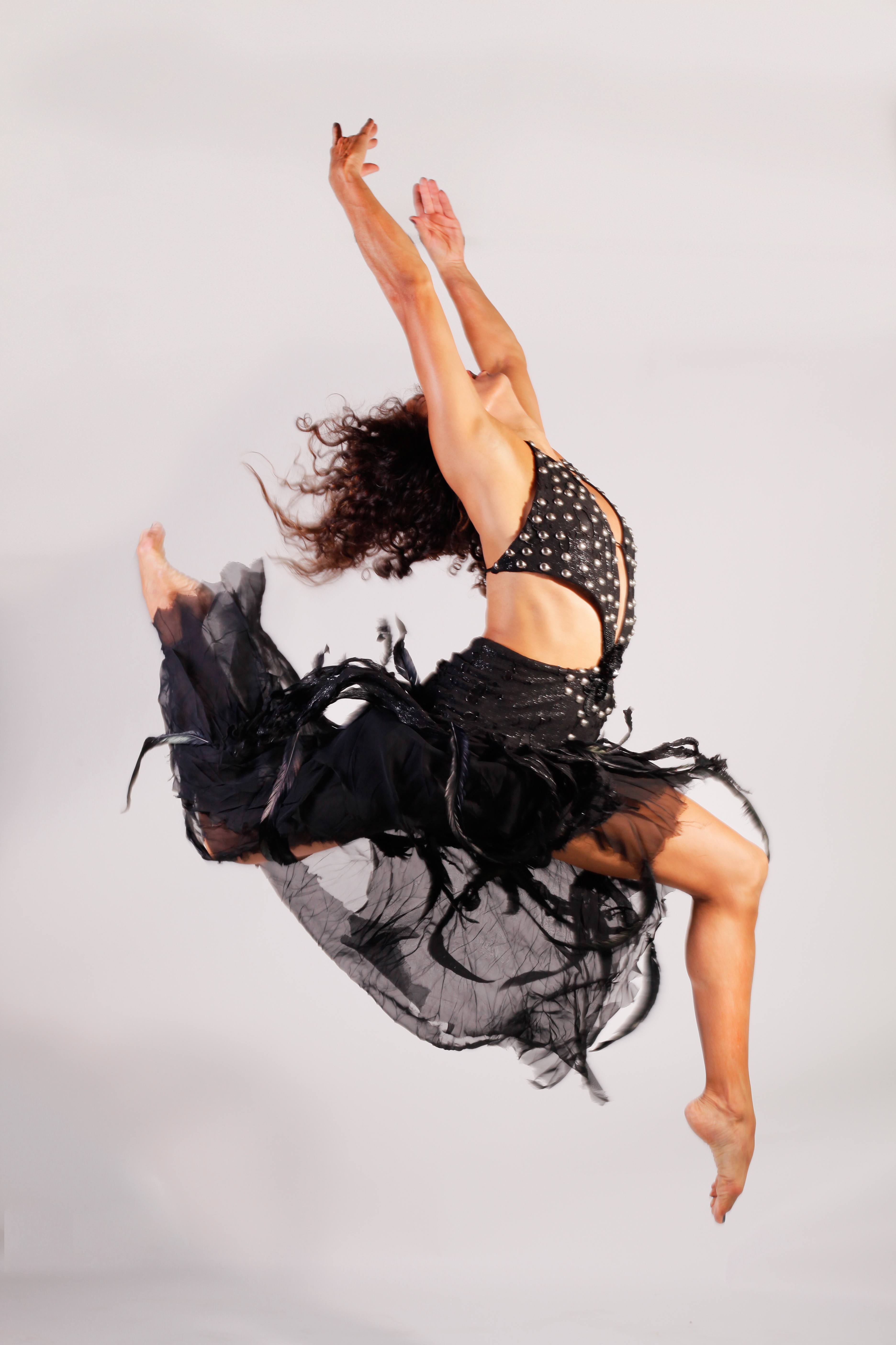 A woman performs a handstand with legs extended upward and arms supporting her body, wearing a black and gold outfit, against a plain background.