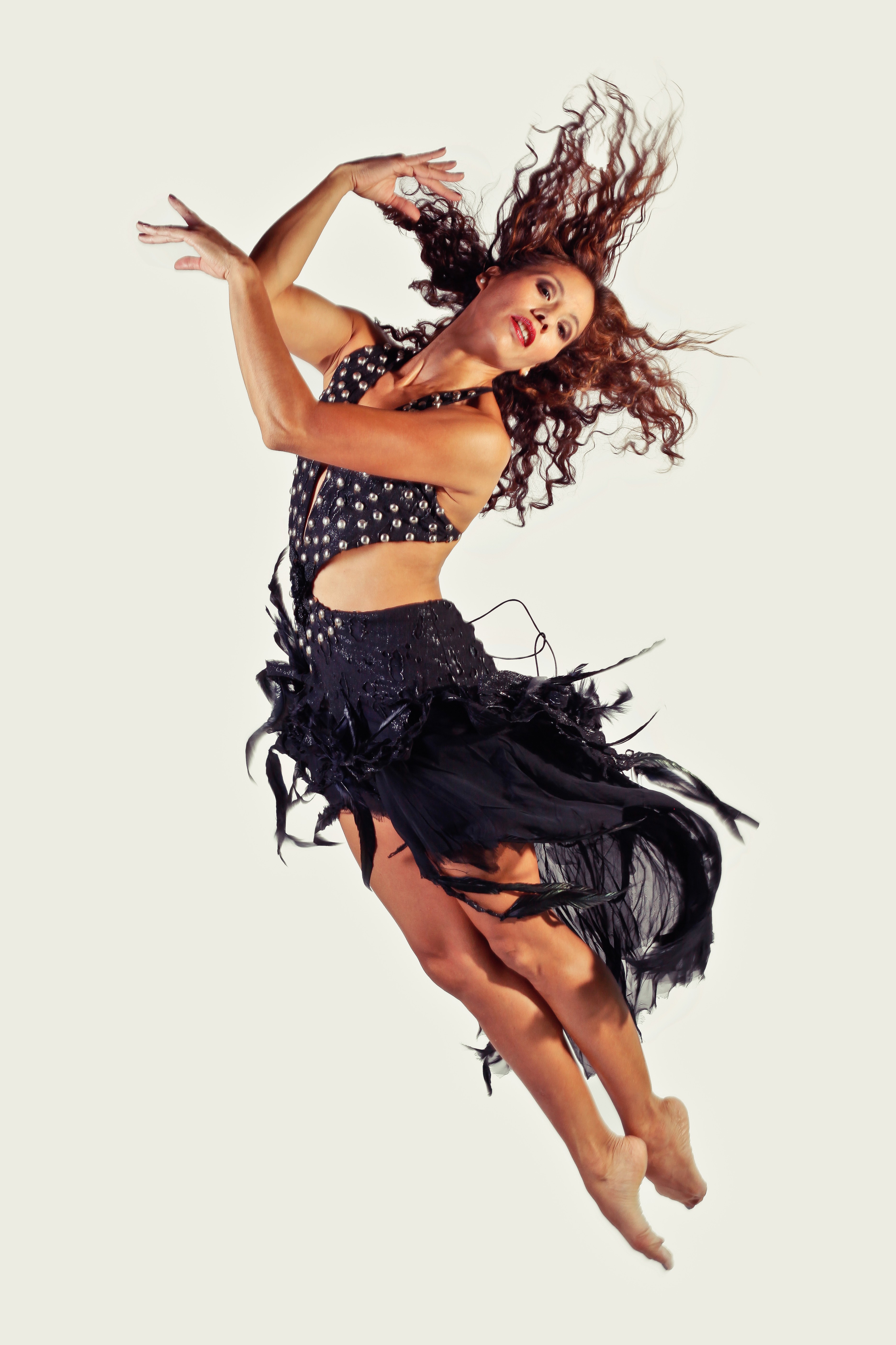Woman dancing with flowing hair, wearing a polka dot top and black skirt, mid-movement against a plain background.