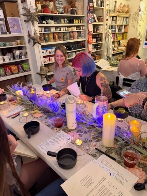 People gathered around a table with candles, flowers, and papers in a cozy room, some with colorful hair, engaging in conversation.