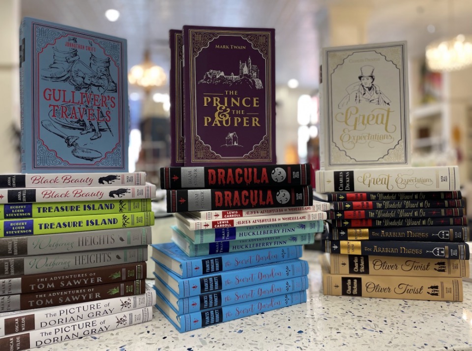 Stack of books and three larger books standing upright on a table, with a blurred background.