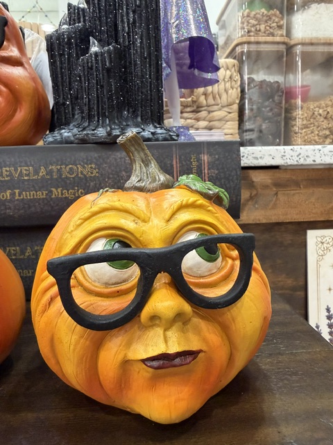 Pumpkin with glasses and lips, placed on a table with books in the background.