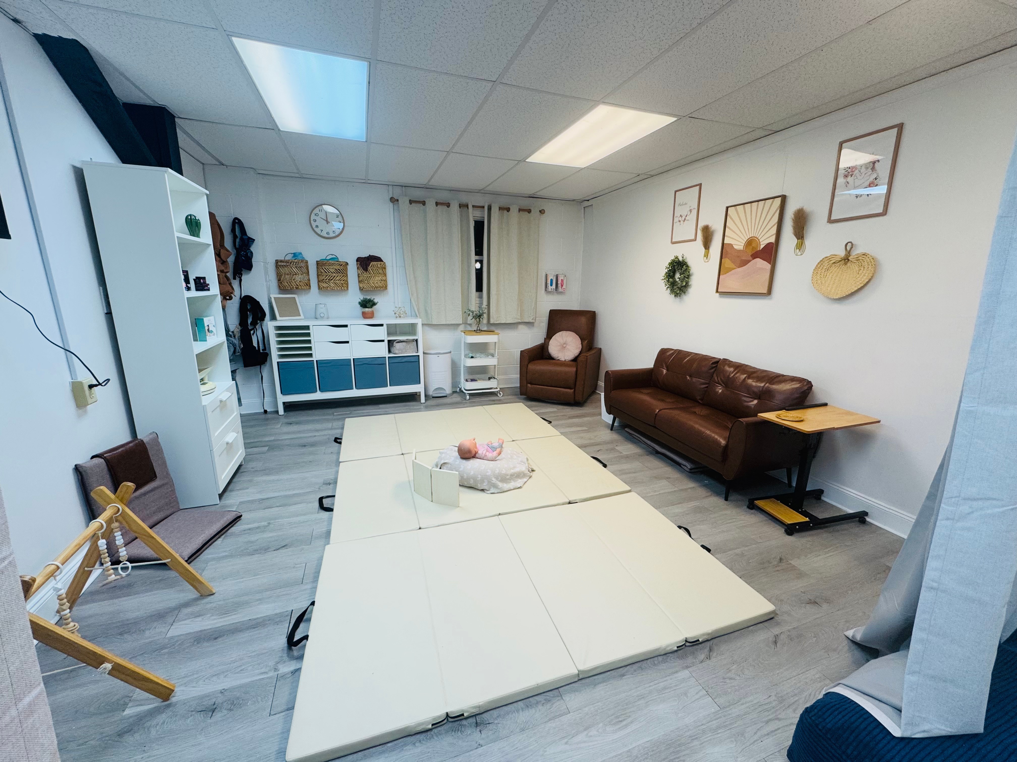Room with white walls, brown leather sofa, armchair, and wall art, with a white folding table and storage units.