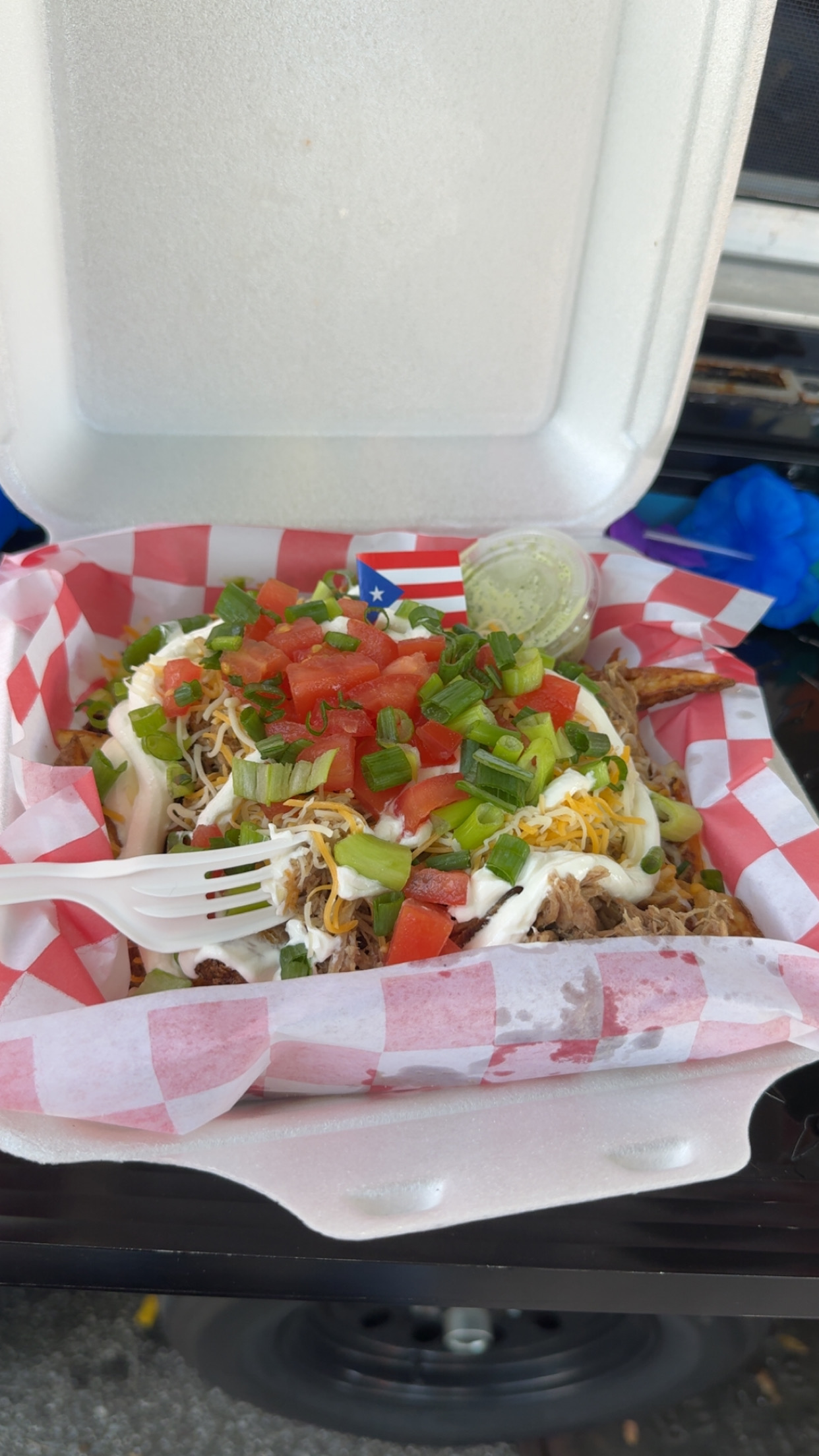 Tacos with lettuce, tomatoes, and sour cream on checkered paper, with a fork and lime wedge, in a takeout container.