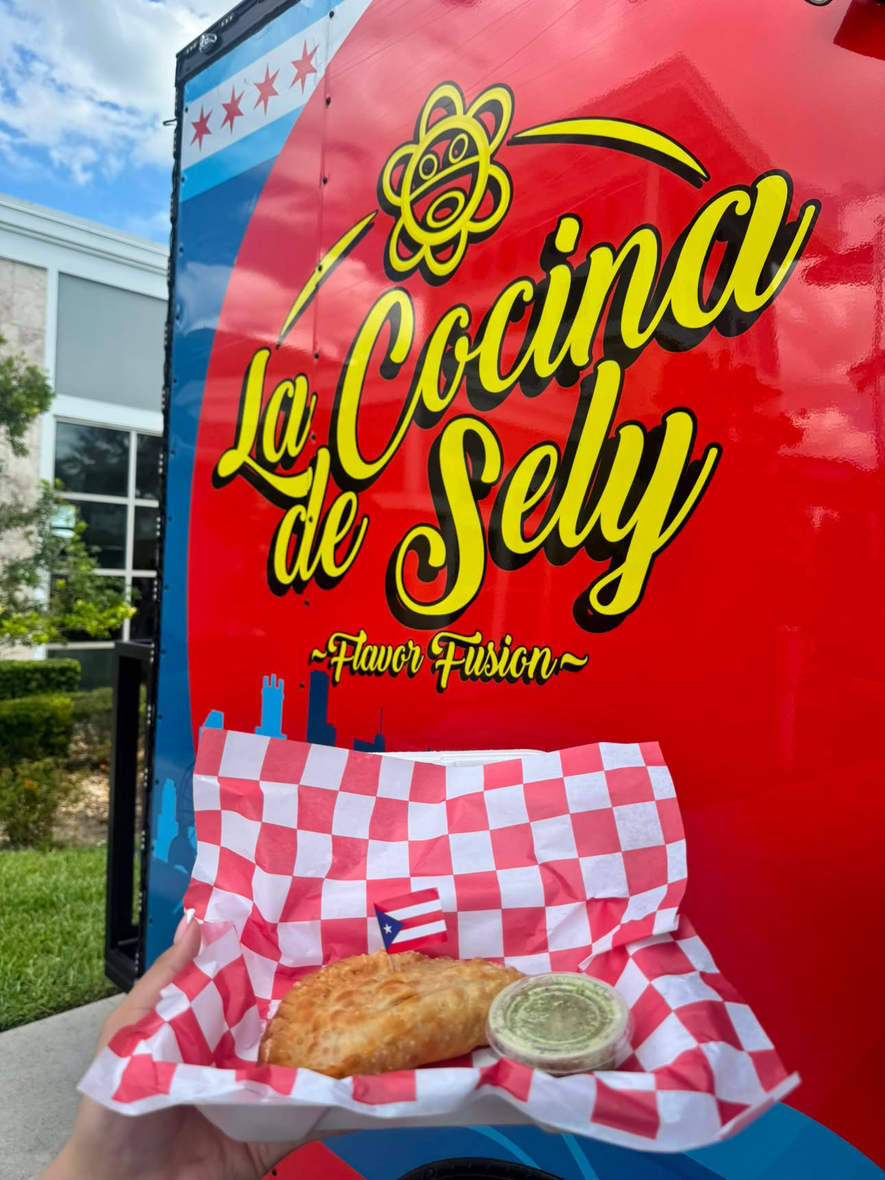 Food item on red and white checkered paper with green sauce, in front of a colorful sign reading La Cocina de Sely.