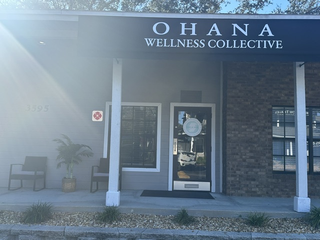 Storefront with sign 'OHANA WELLNESS COLLECTIVE', entrance door, window, bench, and potted plant outside.