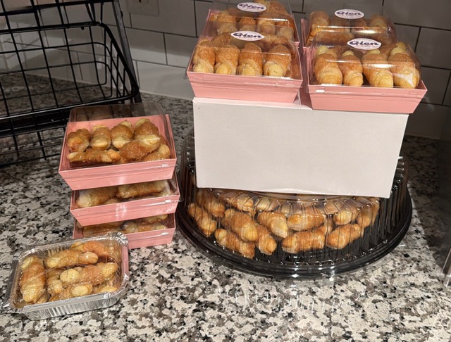 Assorted baked goods in pink and clear containers on a granite countertop, with a black wire basket nearby.