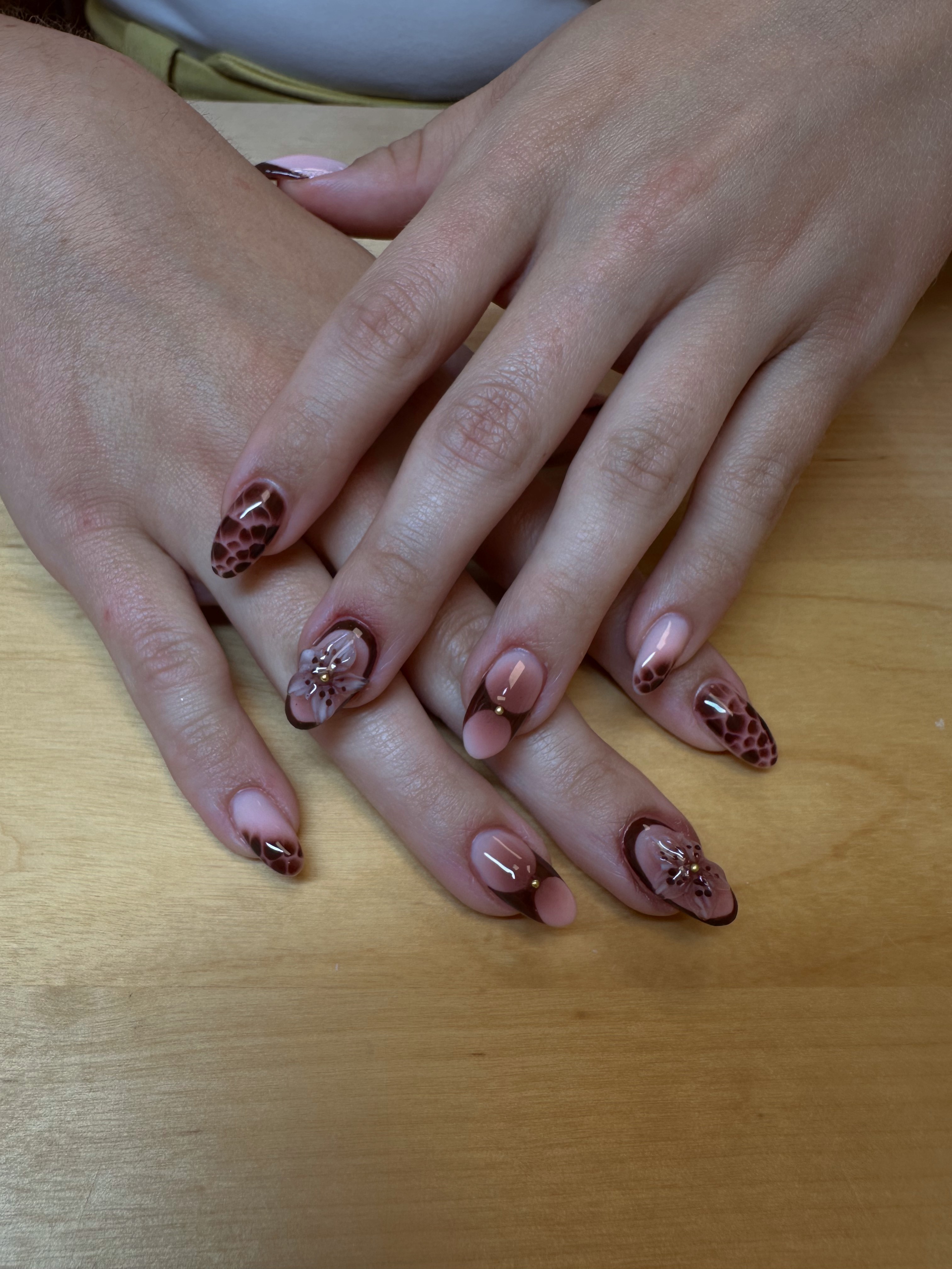 Two hands with decorated nails resting on a wooden surface, showing detailed nail art with animal print and embellishments.